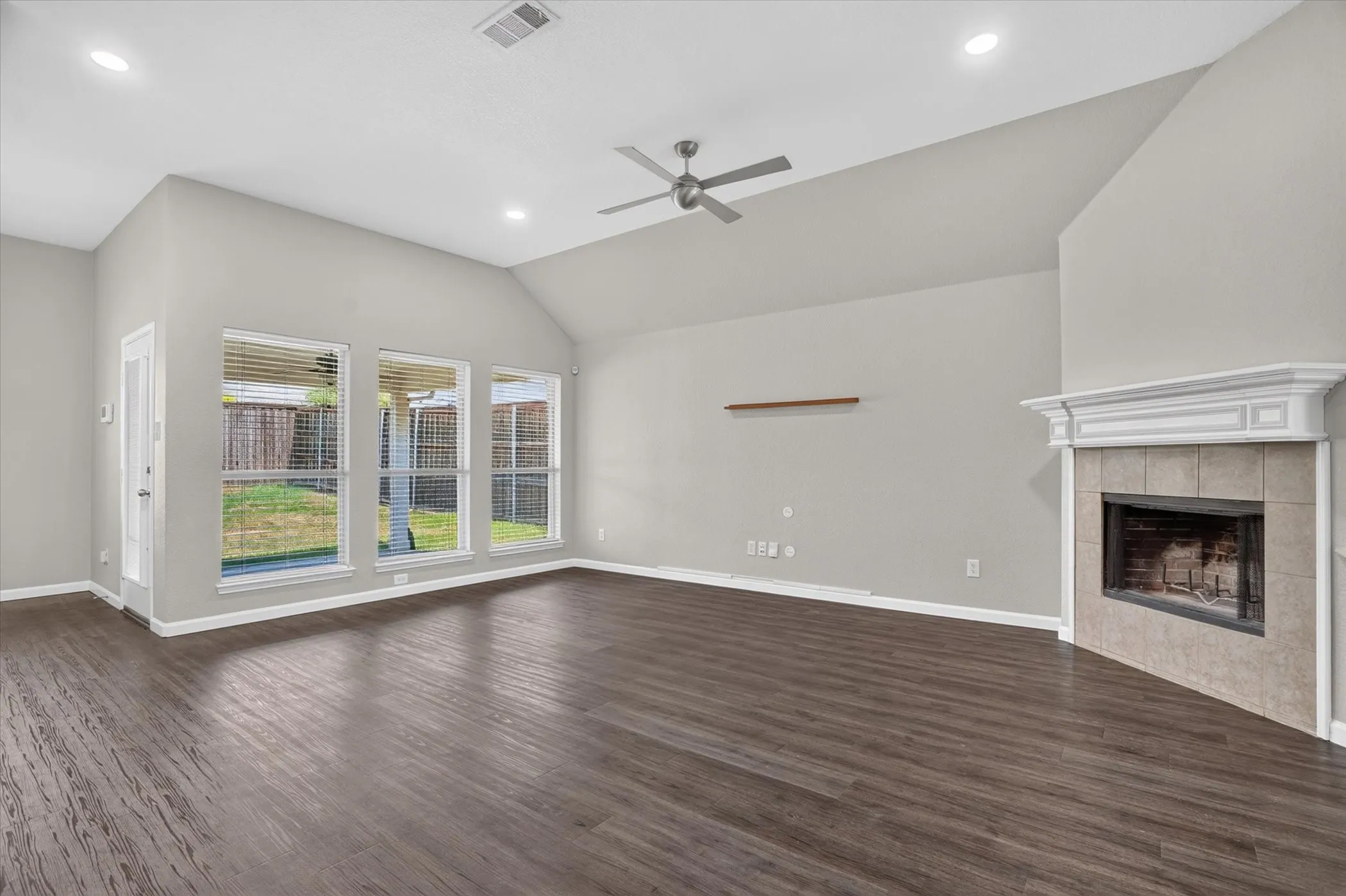 Virtually staged Integrated kitchen and living area, featuring a decorative fireplace with a mantel, dark wood-finish flooring, white cabinetry, and a ceiling fan