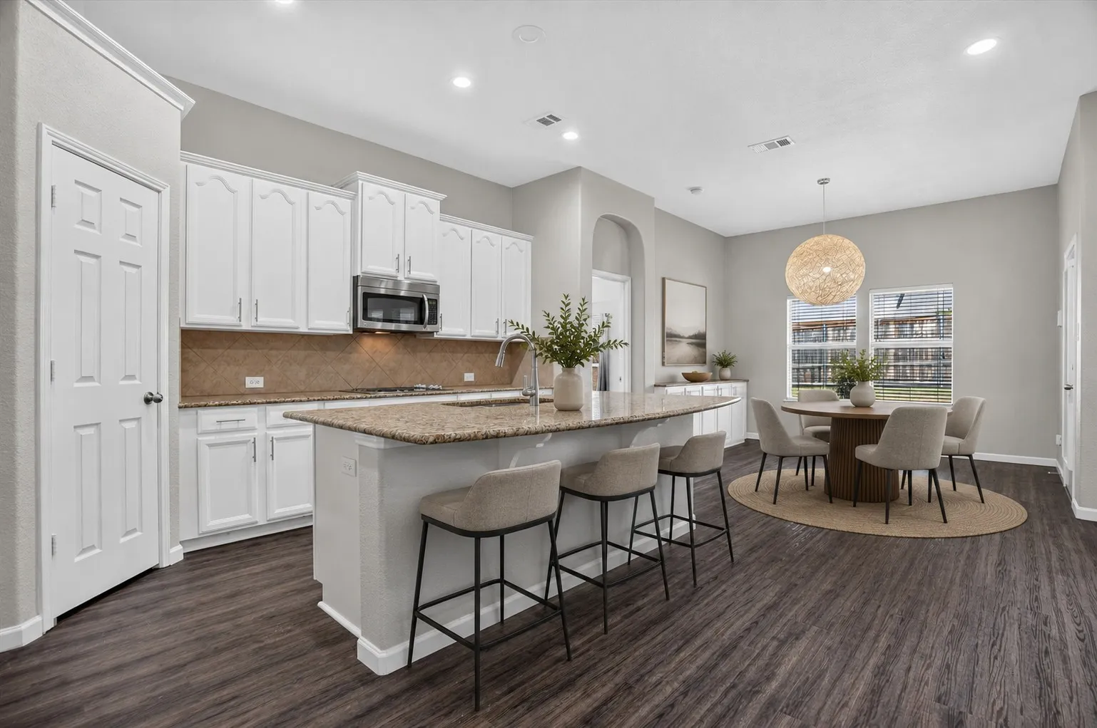 Virtually staged Kitchen island with integrated seating, white cabinetry, integrated stainless steel microwave, wood-finish flooring, and recessed lighting