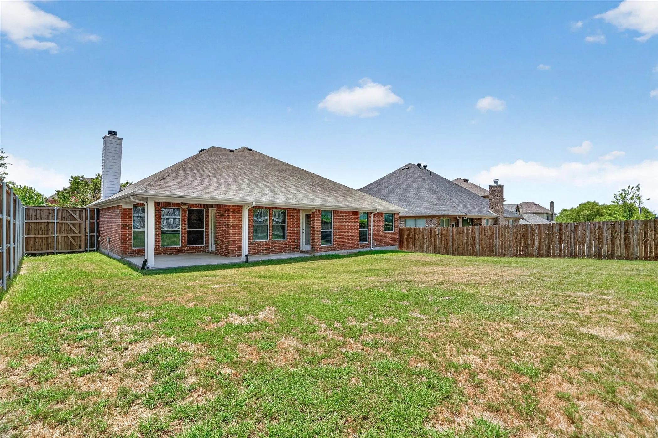 Expansive backyard featuring a covered patio, brick exterior, and a privacy fence