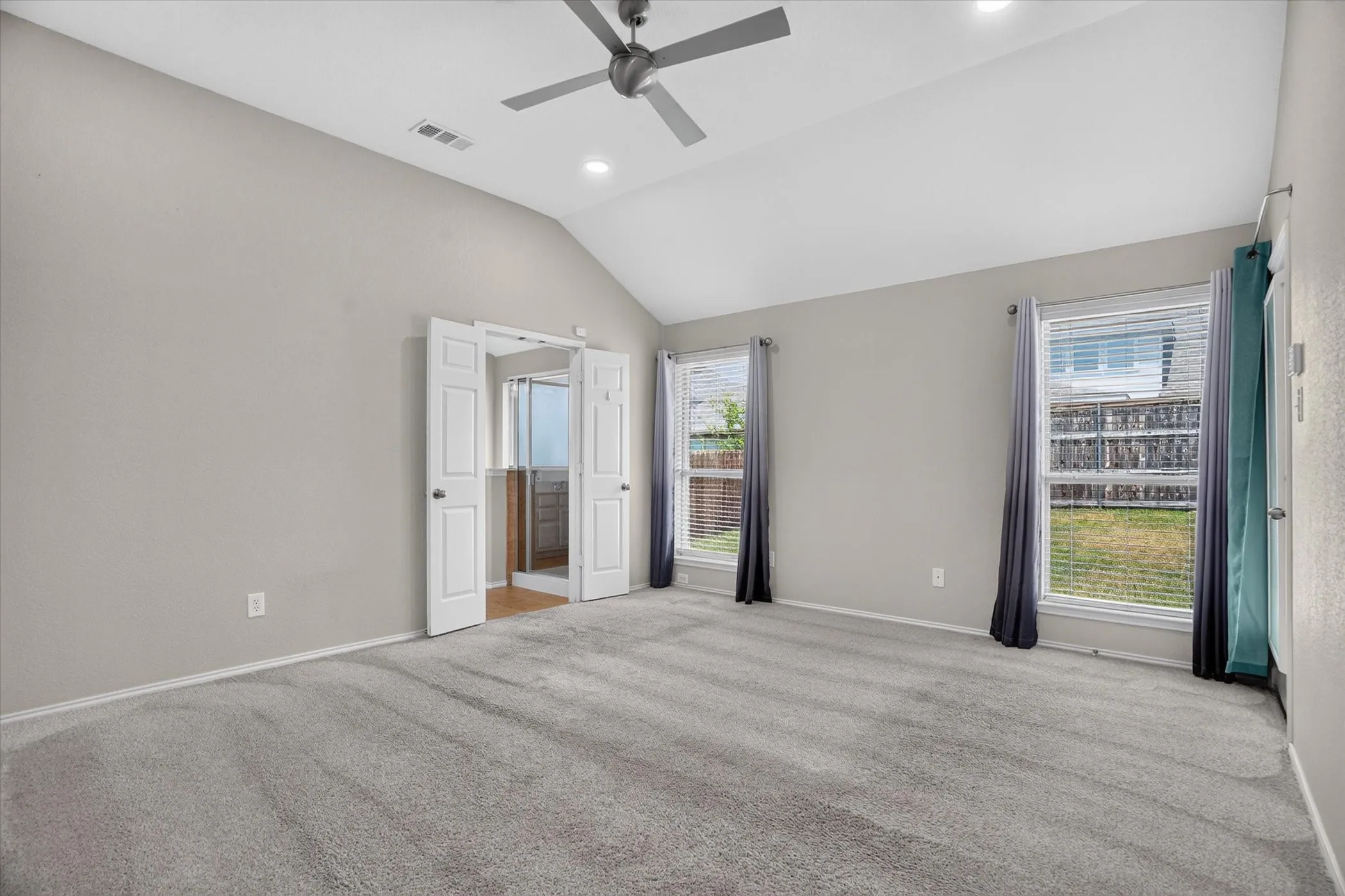 Spacious primary suite featuring vaulted ceilings, recessed lighting, and a ceiling fan