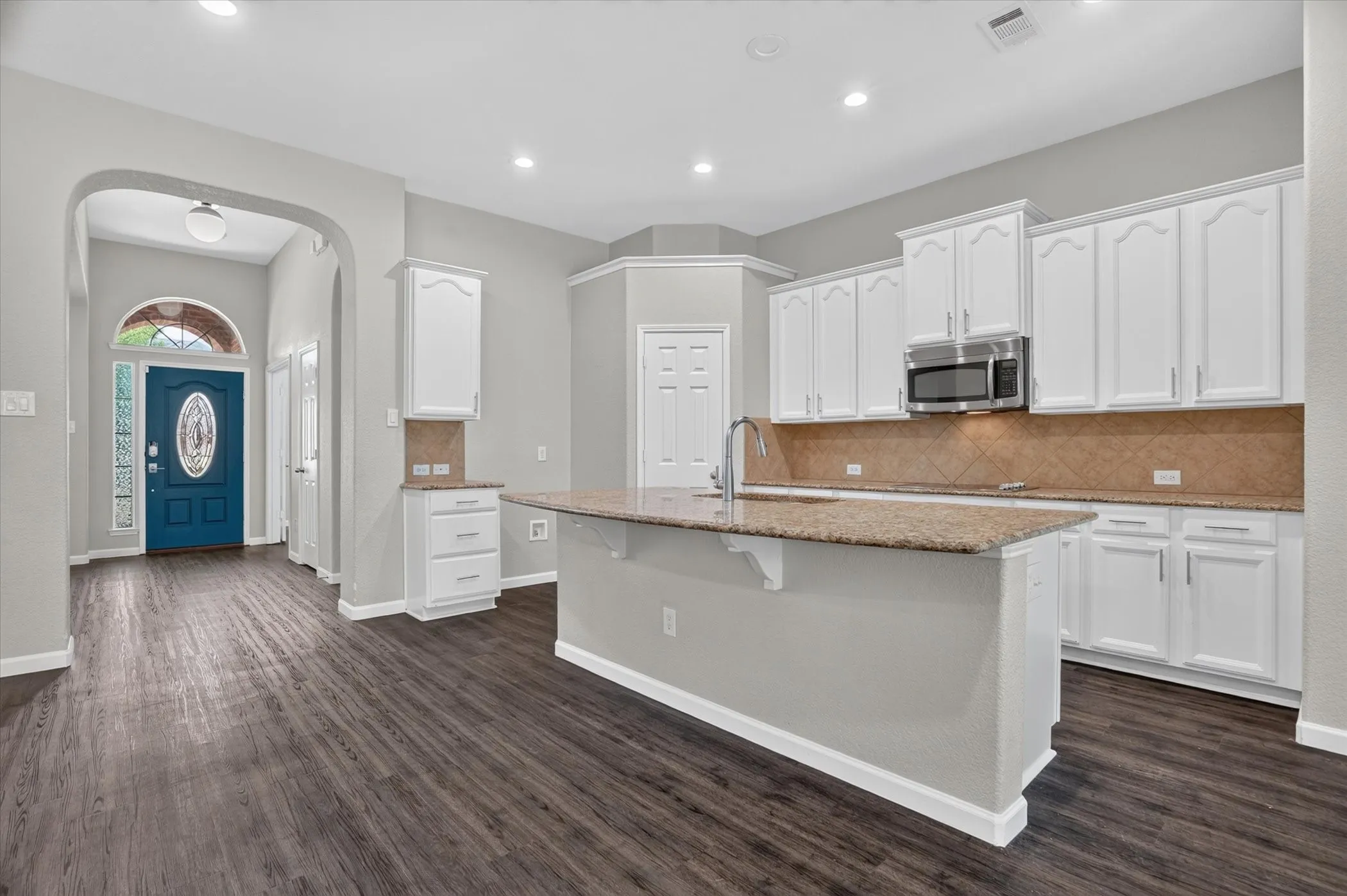 Open-concept kitchen featuring white cabinetry, stainless steel microwave, granite countertops, and wood-finish flooring