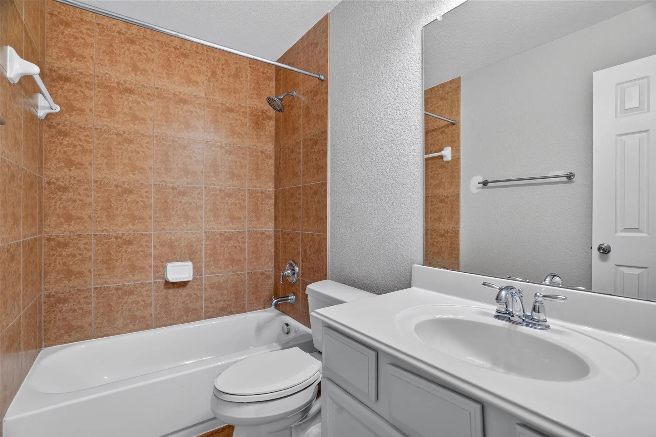 Dual-sink vanity with white cabinetry and chrome fixtures anchors this full bathroom, complemented by warm terracotta tile surround in the shower-tub combination