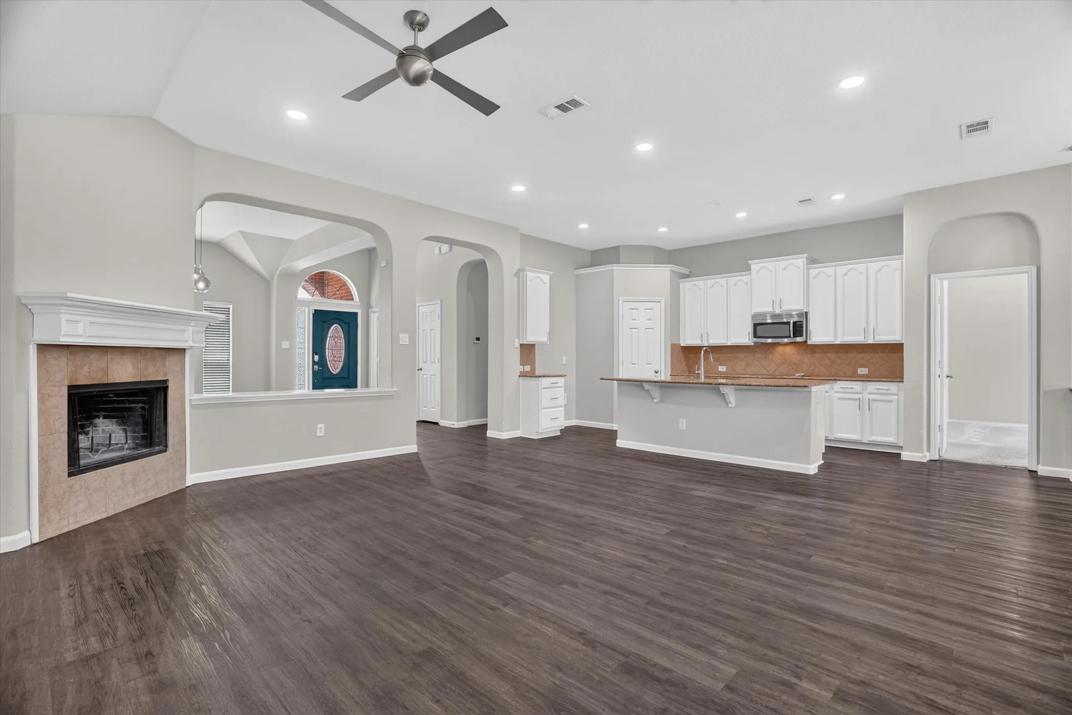Virtually staged Kitchen featuring a large island with stone countertop, white cabinetry with black hardware, stainless steel appliances, and wood-finish flooring