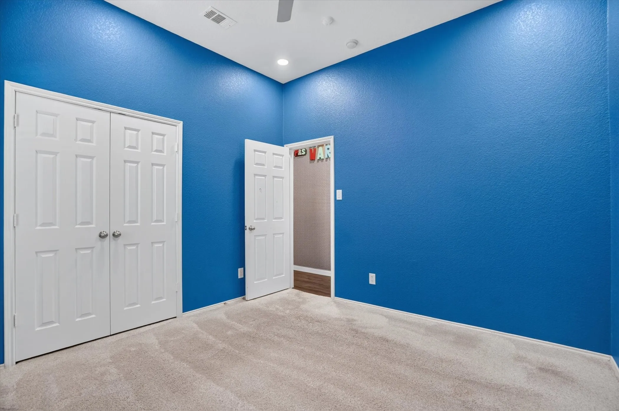 Bright, freshly painted bedroom showcasing vibrant blue walls, neutral carpet flooring, and abundant natural lighting