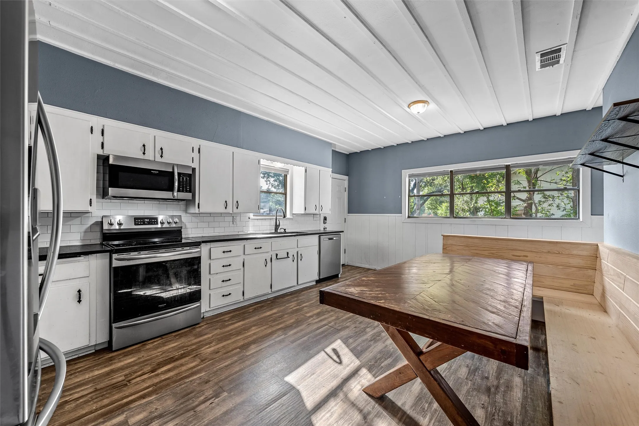 White cabinetry with black countertops, stainless steel appliances, and wood-finish flooring