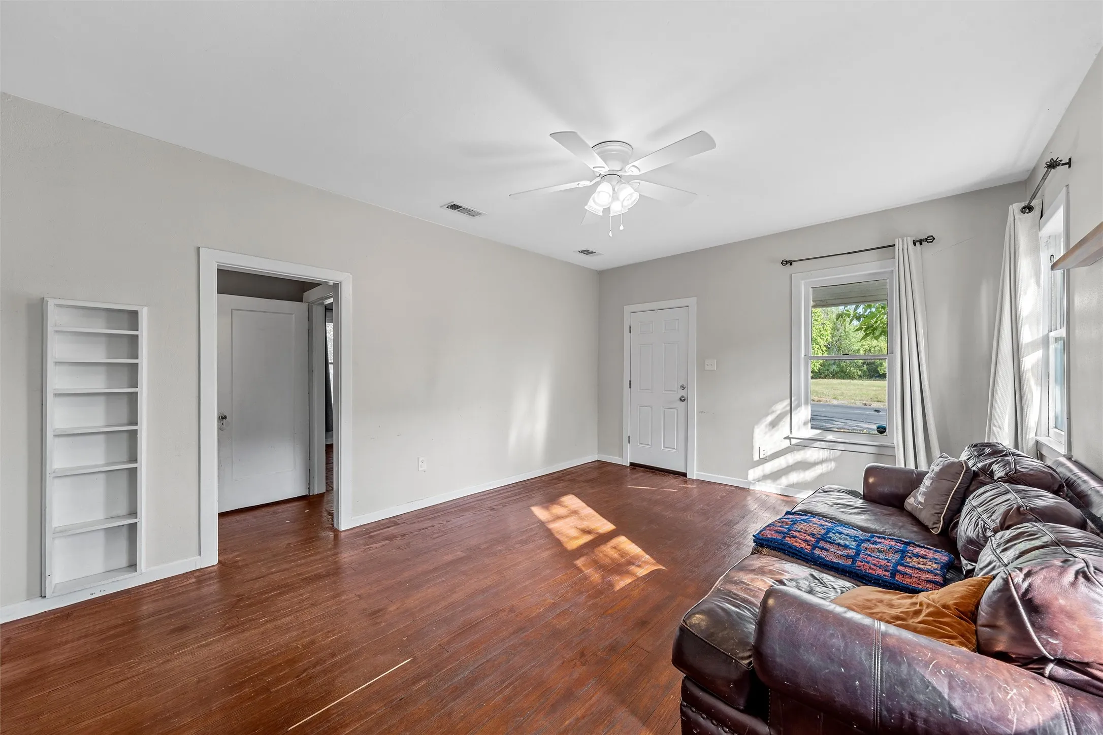 Wood-finish flooring, built-in shelving, white ceiling fan, and white walls