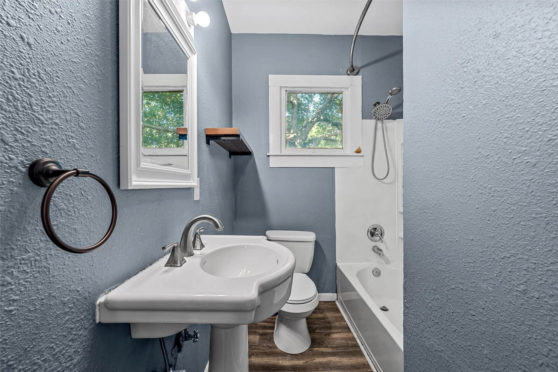 Pedestal sink with a chrome faucet, white-framed mirror, and a built-in bathtub with shower