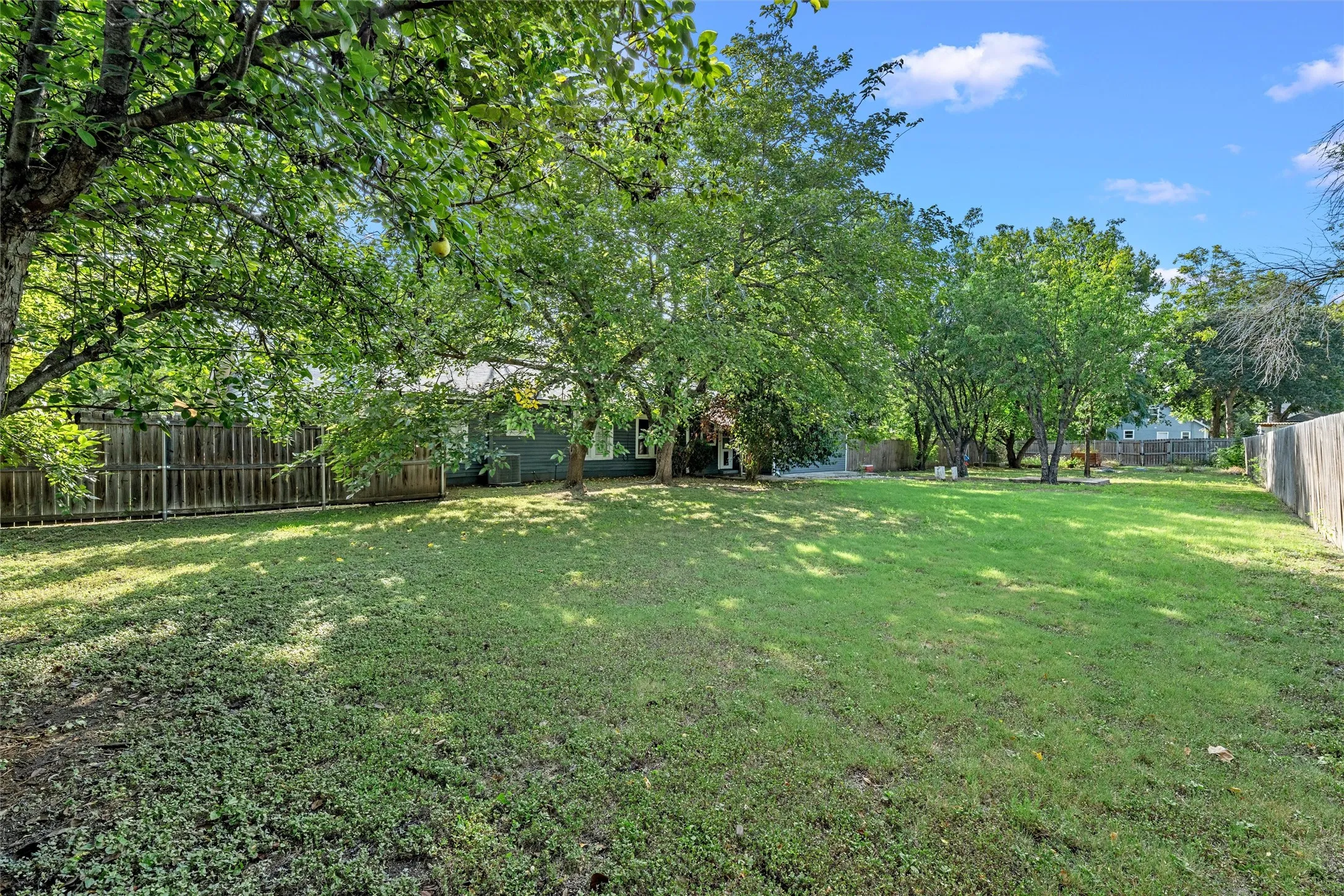 Expansive backyard featuring a lush, manicured lawn shaded by mature trees throughout the property