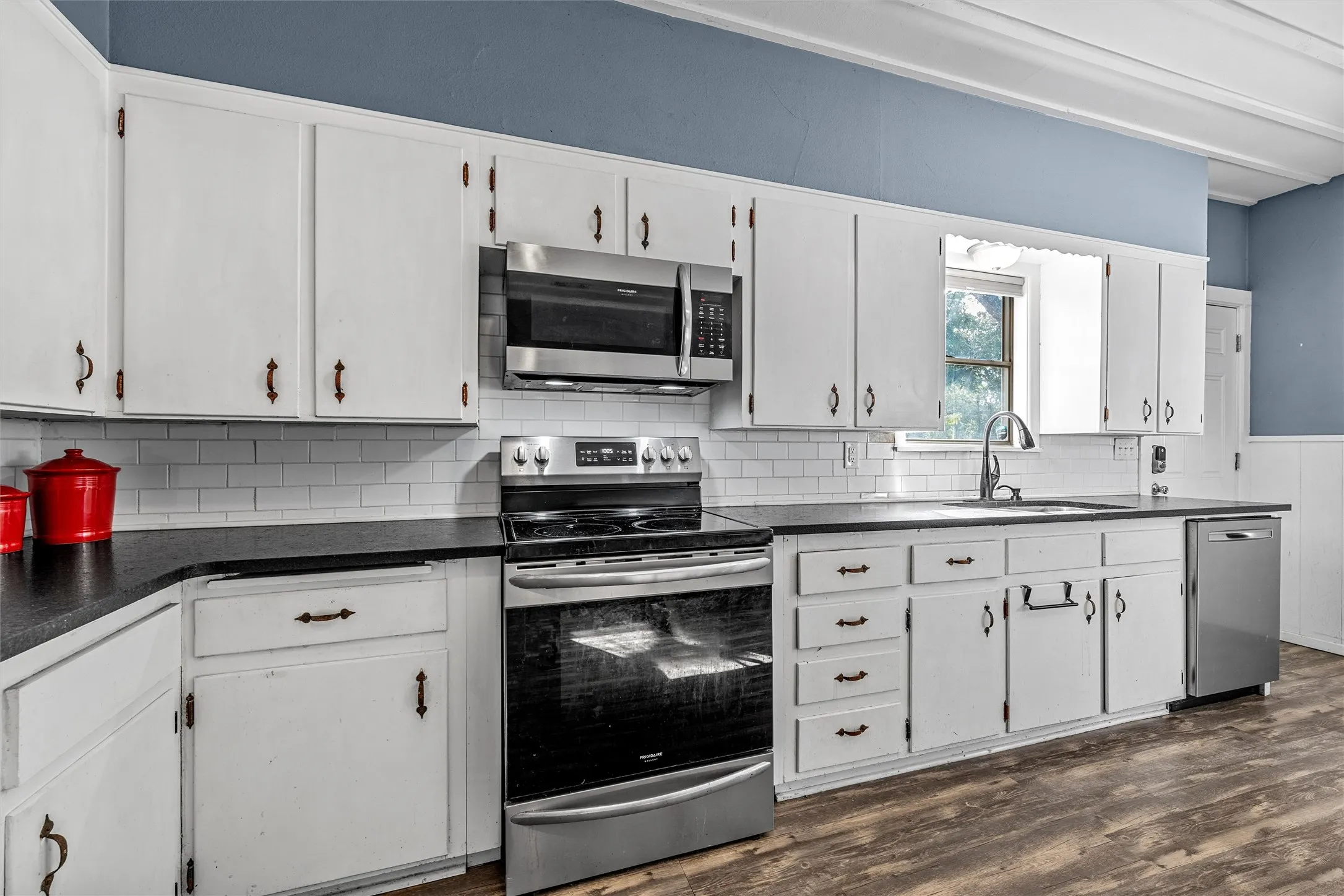 Kitchen featuring extensive white cabinetry, dark countertops, white subway tile backsplash, stainless steel appliances, and wood-finish flooring