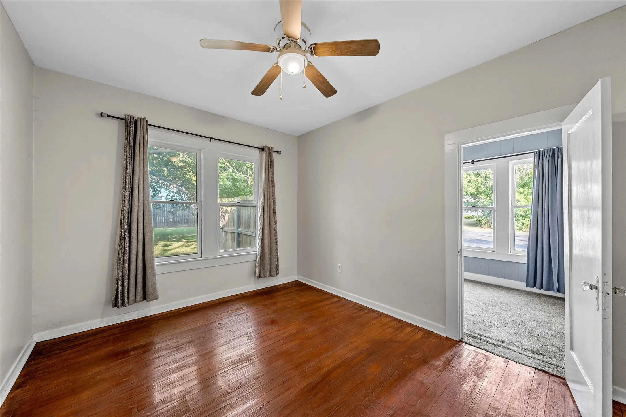 Wood-finish flooring, ceiling fan with integrated lighting, and multiple windows providing natural illumination