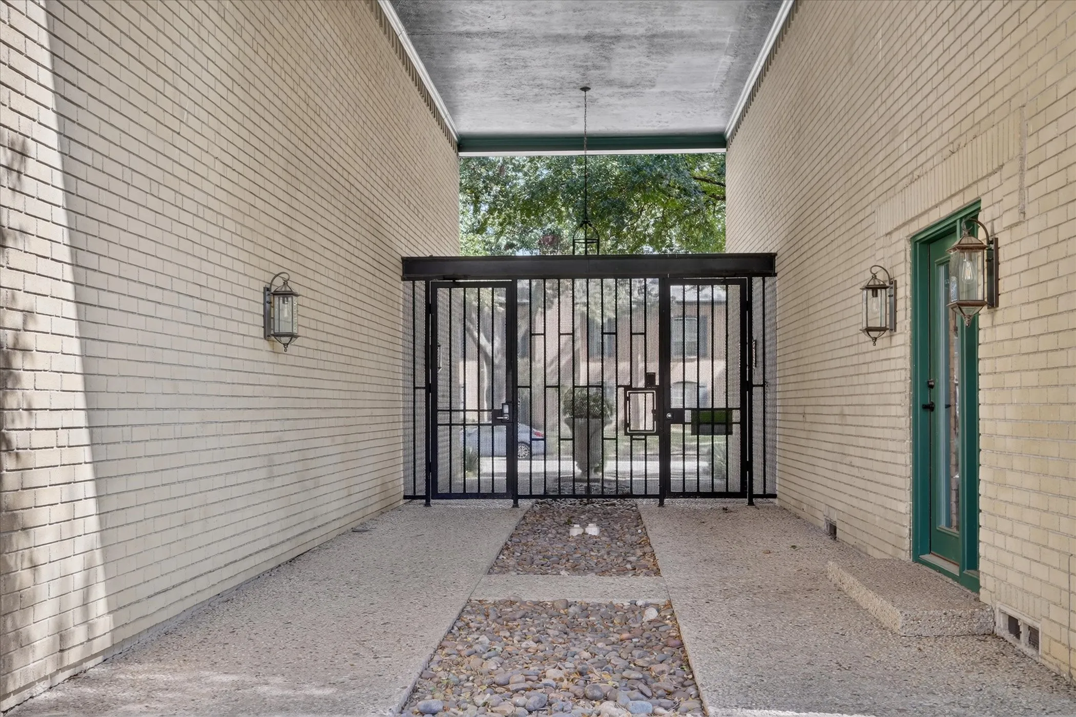 Private gated entry courtyard at 6020 E University Blvd Dallas TX 75206. Covered passage with iron gate, pendant lighting, and direct unit access.