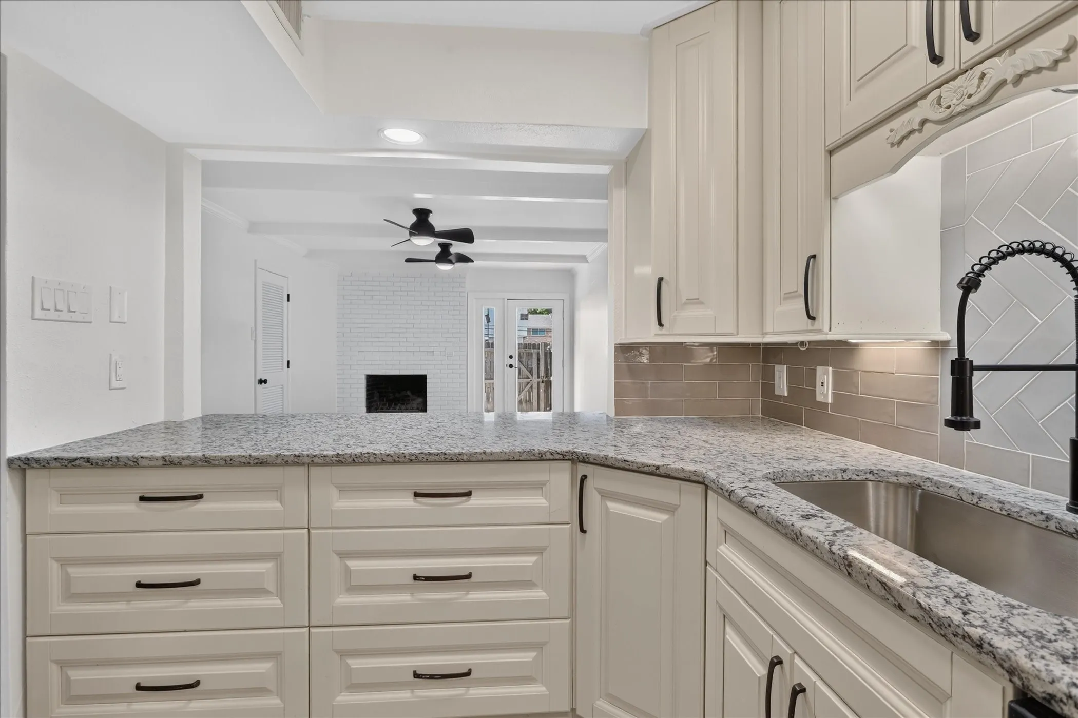 New kitchen peninsula with granite countertops at 6020 E University Blvd Unit 117 Dallas. Open to living room with white brick fireplace, painted beam ceilings, and French doors.