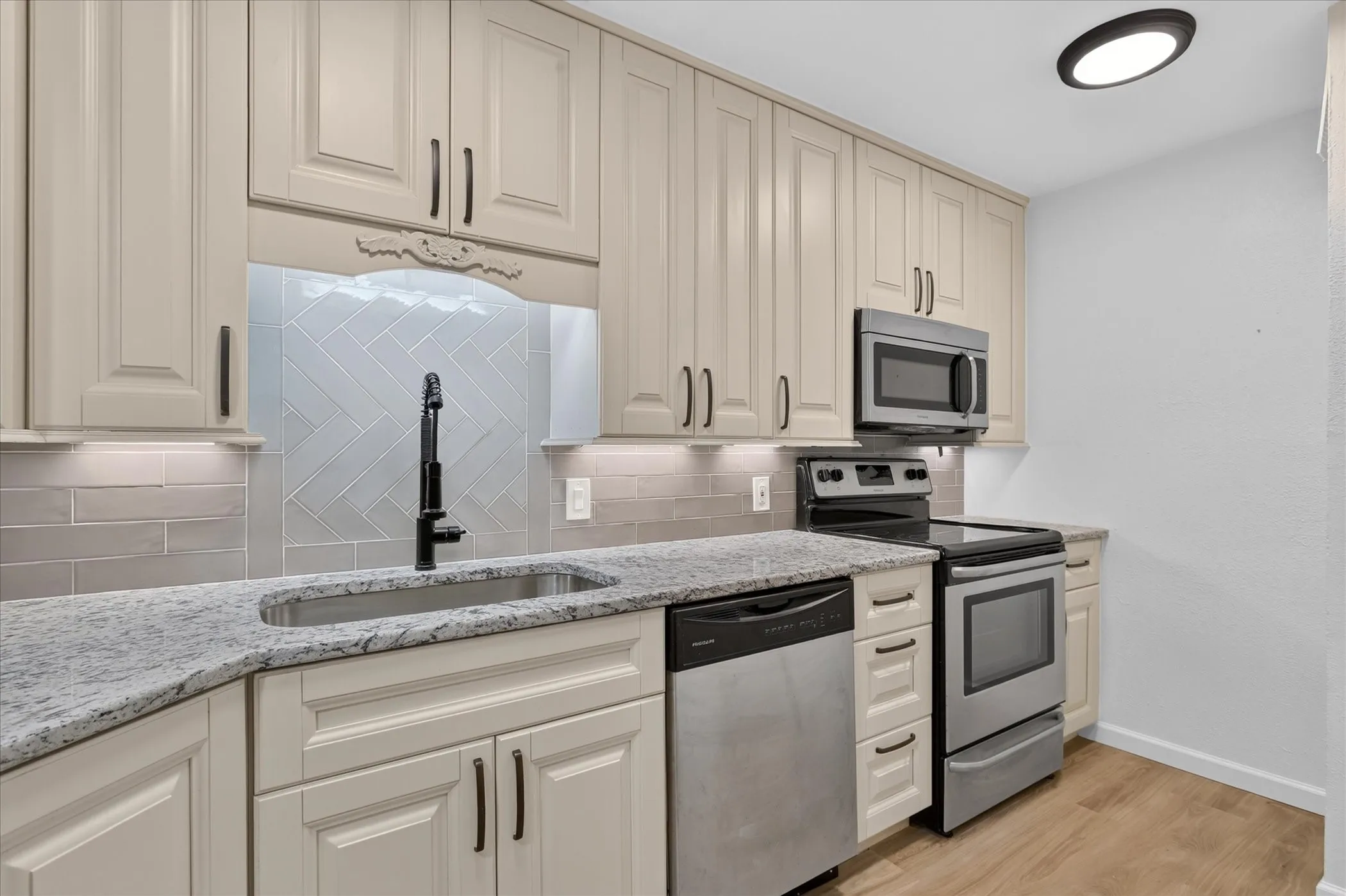 Renovated kitchen at 6020 E University Blvd Unit 117. New cream raised-panel cabinetry, granite countertops, herringbone tile backsplash, and stainless Frigidaire appliances.