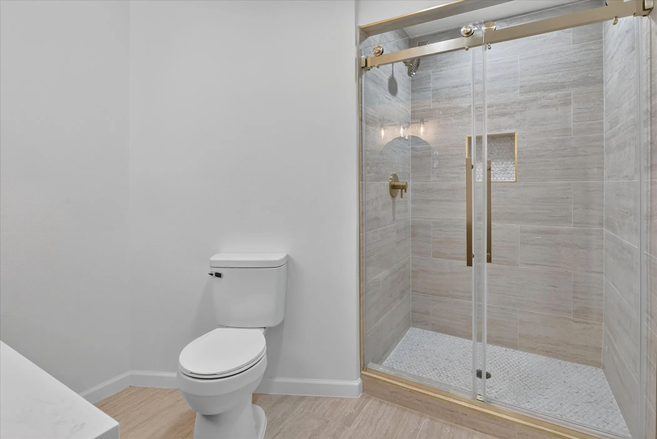 Walk-in shower at 6020 E University Blvd Unit 117 Dallas — gold sliding glass door, large format tile walls, mosaic tile floor pan, gold fixtures, and built-in niche.