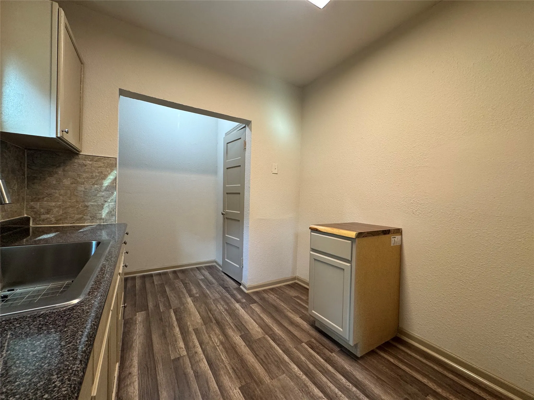 Galley kitchen featuring stainless steel appliances, granite countertops, subway tile backsplash, wood-finish flooring, and ample cabinetry with overhead storage