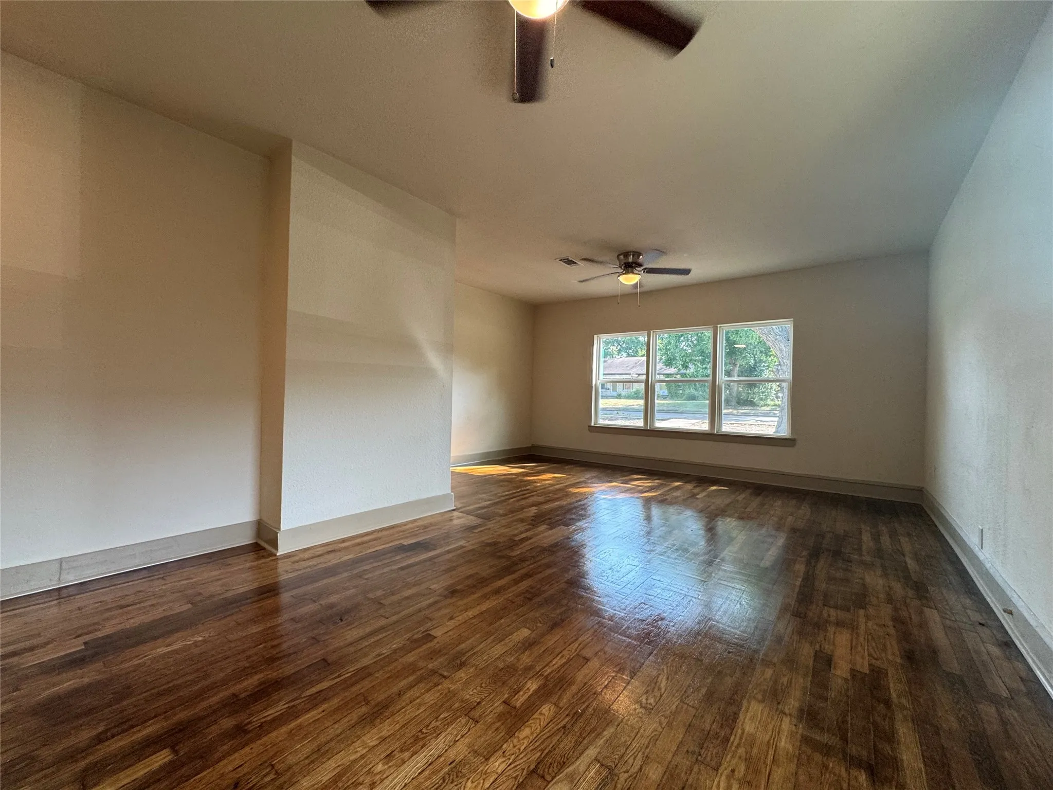 Hardwood-style flooring, three large windows, two ceiling fans, and neutral wall finishes