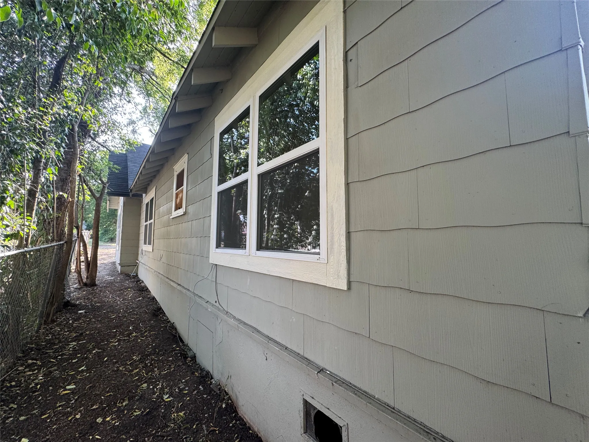 Charming cottage-style home featuring horizontal fiber cement siding, large multi-pane windows with white trim, and mature tree-lined landscaping along the side elevation