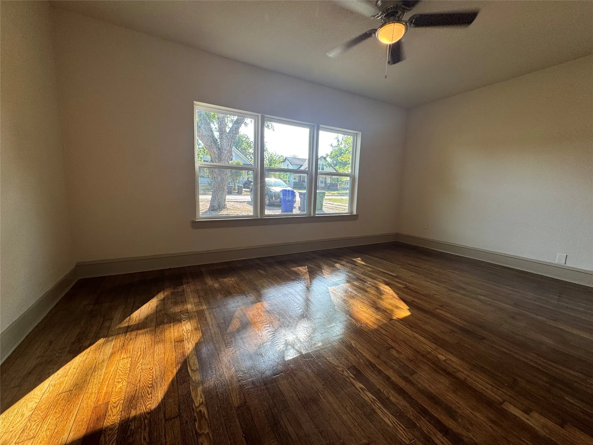 Hardwood flooring, triple window arrangement, ceiling fan with integrated lighting, and neutral wall tones