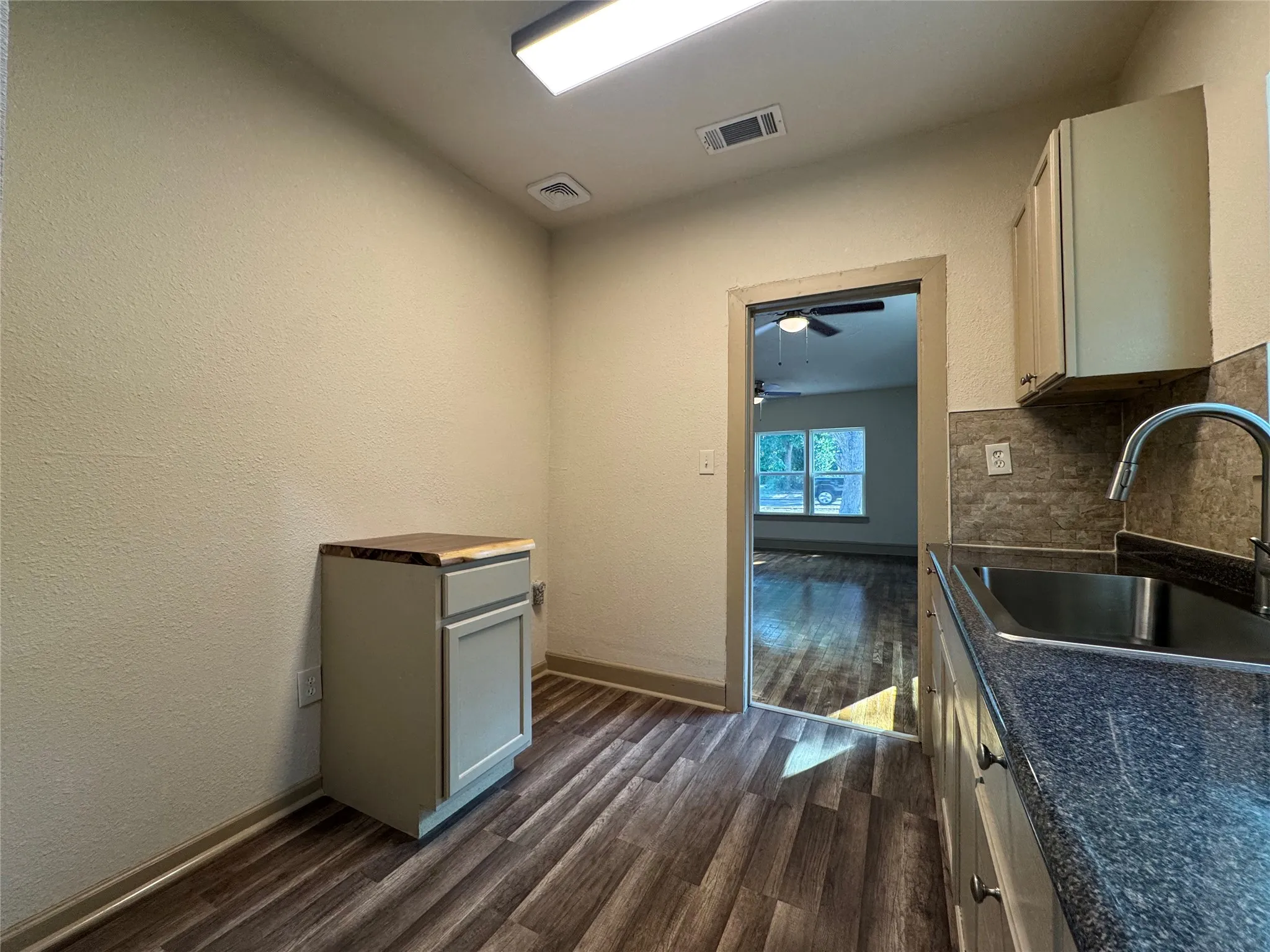 Modern kitchen featuring stainless steel sink with gooseneck faucet, wood-finish flooring throughout, granite-style countertops, white cabinetry with ample storage, and glass tile backsplash accents