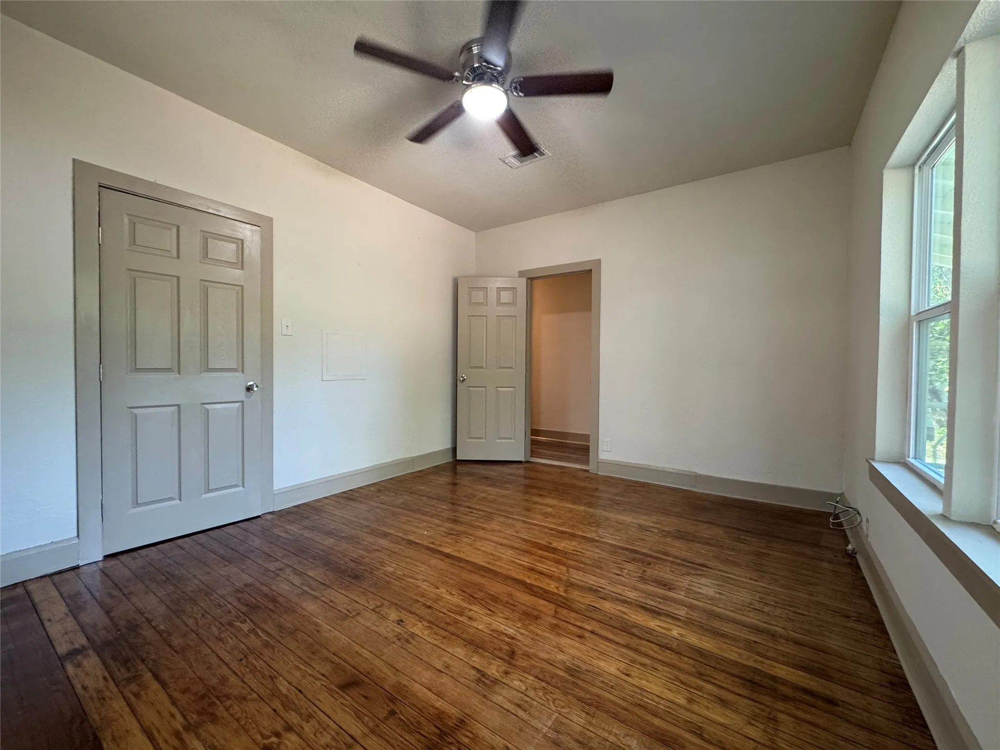 Hardwood flooring, ceiling fan with integrated lighting, paneled doors, and natural light from a window