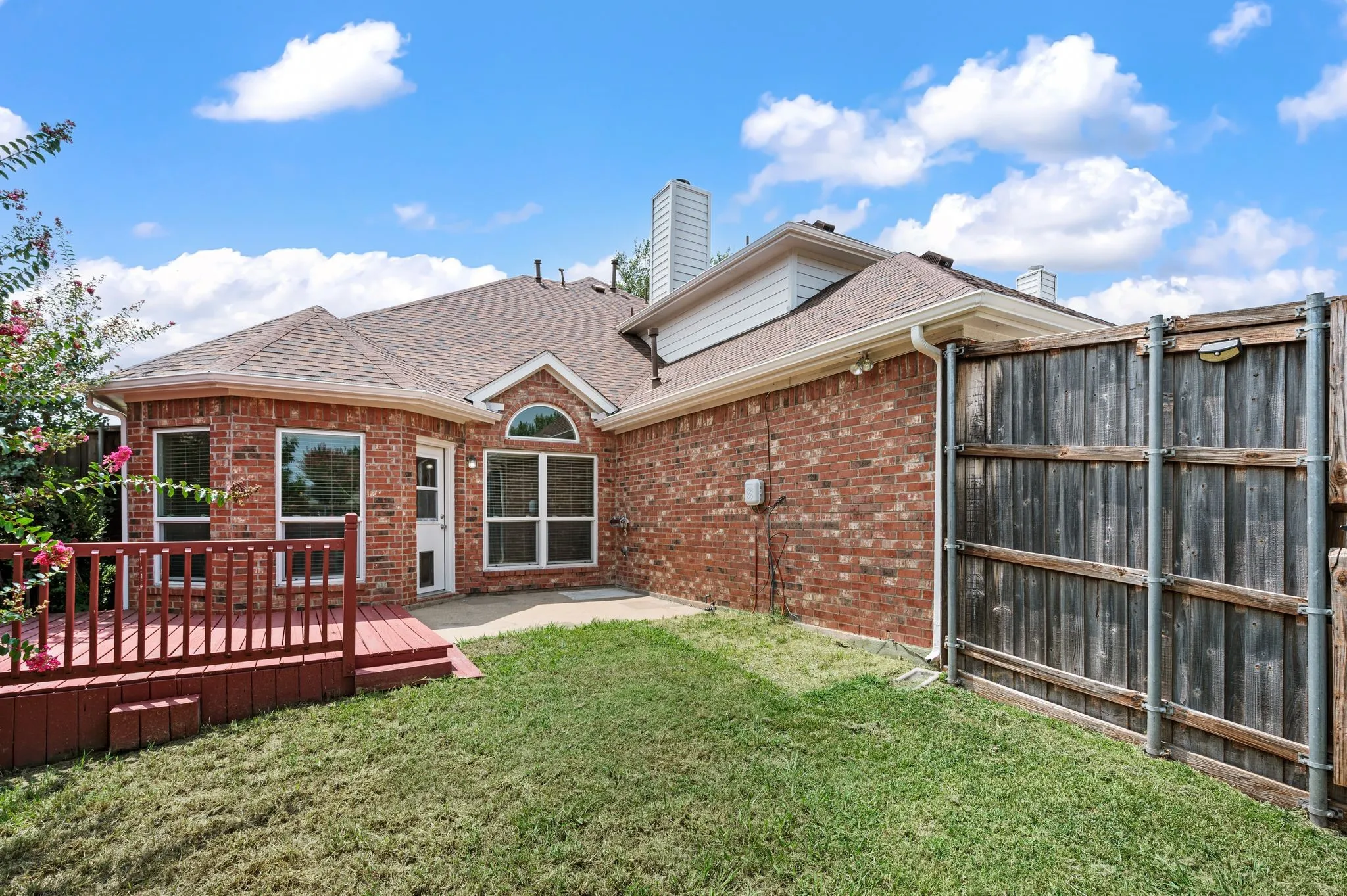 Brick exterior featuring a wood deck with red railing, multiple windows, and a partial privacy fence