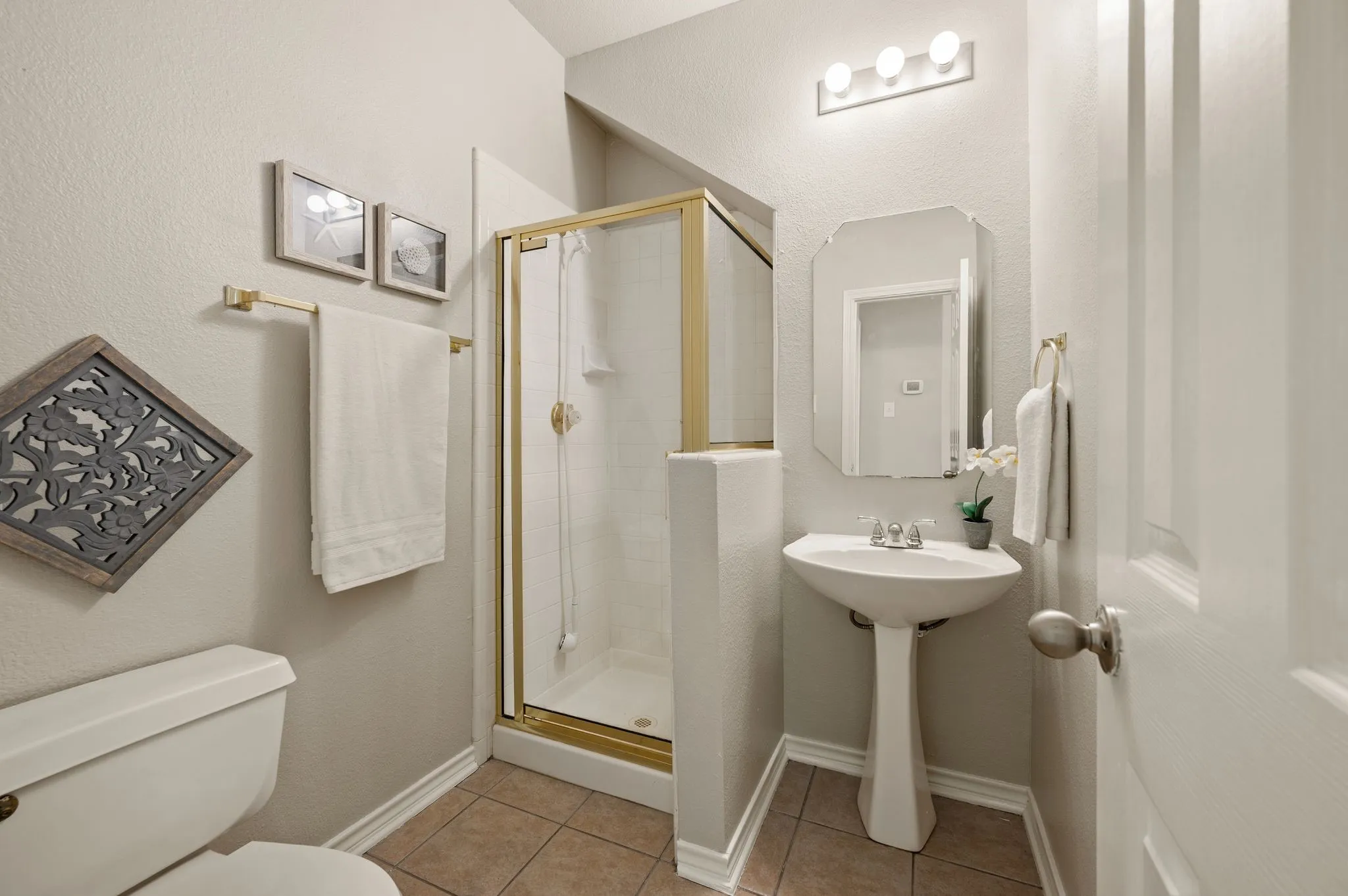 Bathroom featuring a pedestal sink, framed mirror, and a shower with a gold-tone enclosure