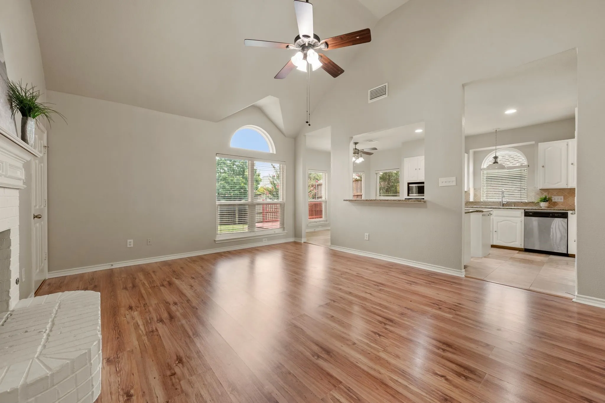 Spacious living area featuring high vaulted ceilings, wood-finish flooring, and a whitewashed brick fireplace