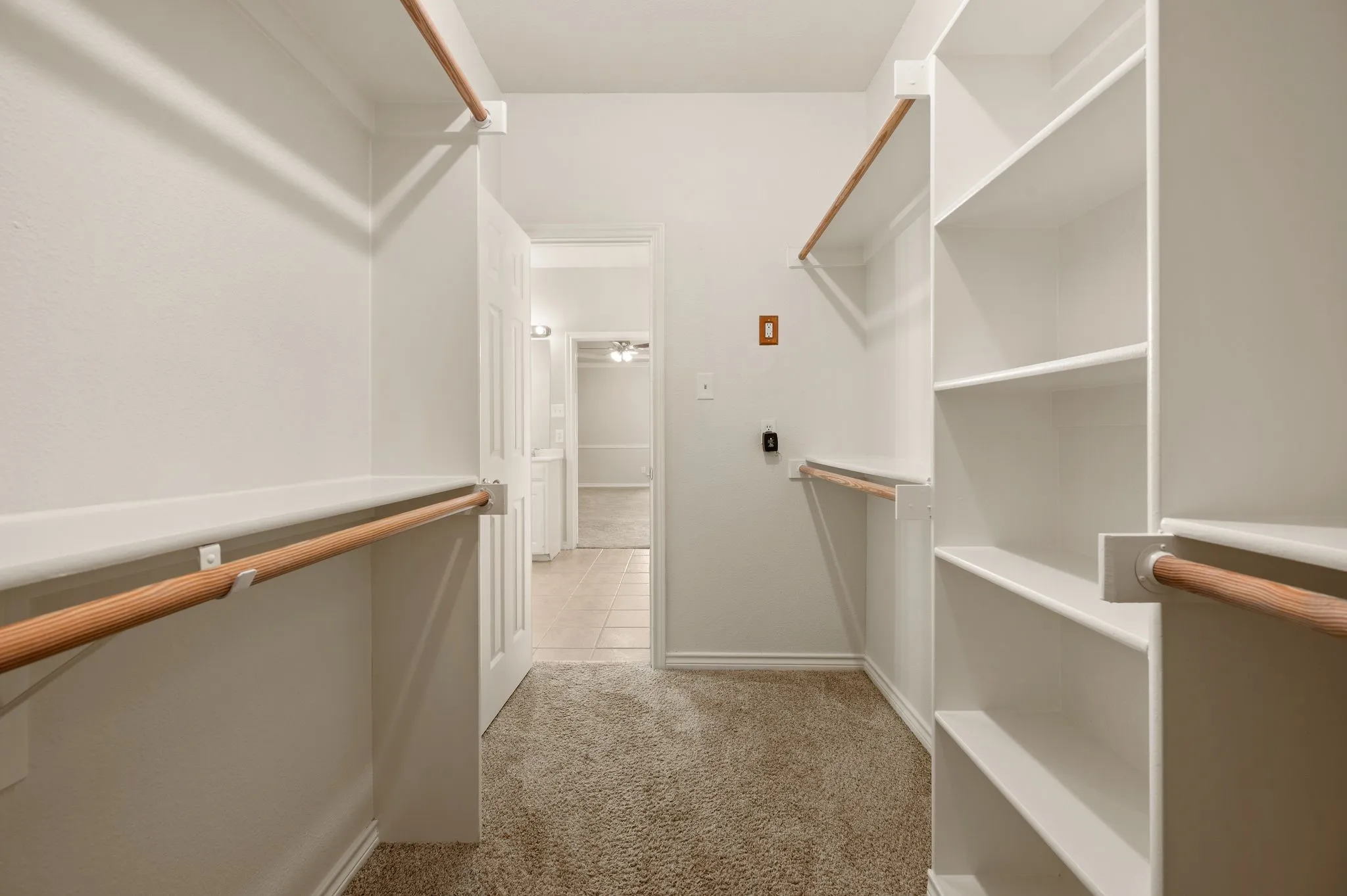 Walk-in closet featuring carpet flooring, built-in shelving, and multiple hanging rods for organization