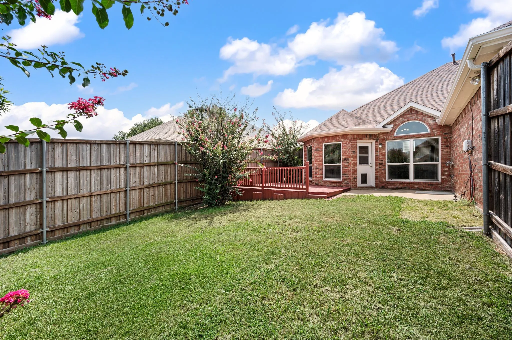 Expansive backyard featuring a manicured lawn, a red-stained wood deck, and a privacy fence
