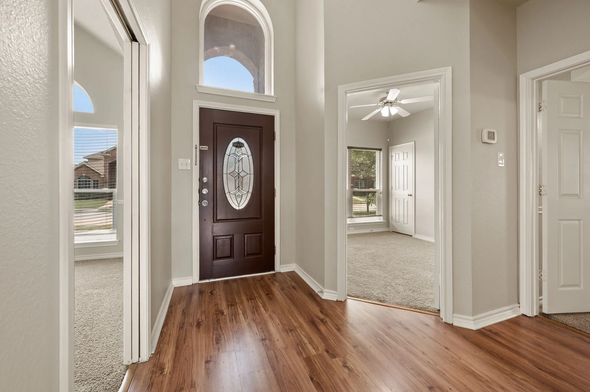 Foyer featuring a dark wood-finish entry door with an oval leaded glass insert, an arched transom window, wood-finish flooring, and light-toned walls