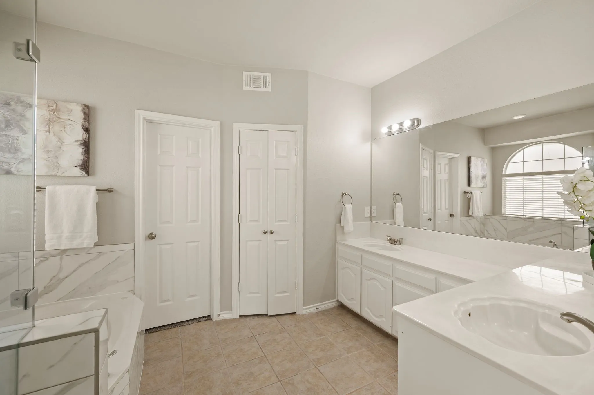 Bathroom with tile flooring, dual vanities with white cabinetry and integrated sinks, and a large mirror extending across both