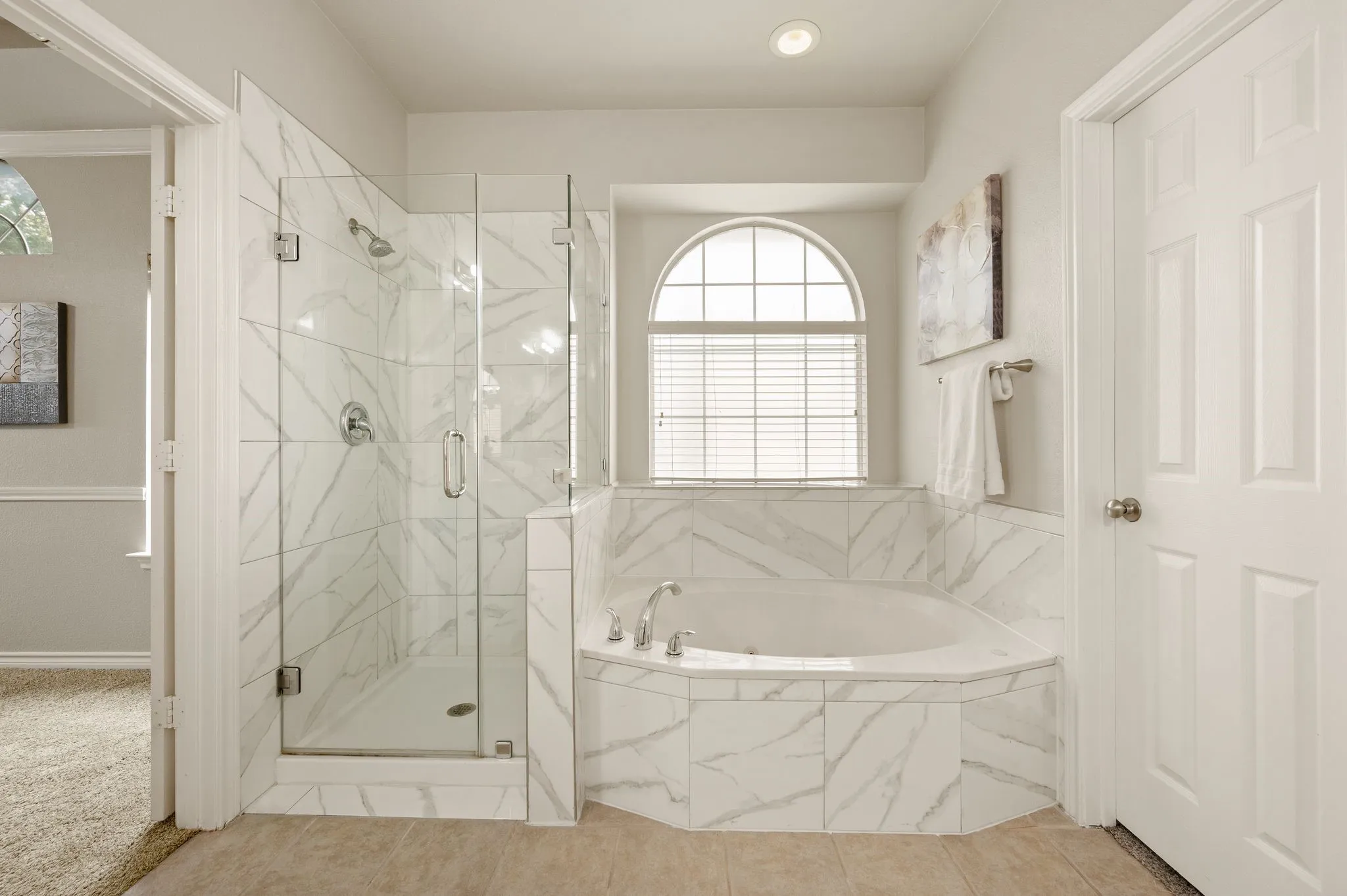 Bathroom featuring a corner soaking tub with marble-look tile surround, a glass-enclosed shower with matching tile, and an arched window