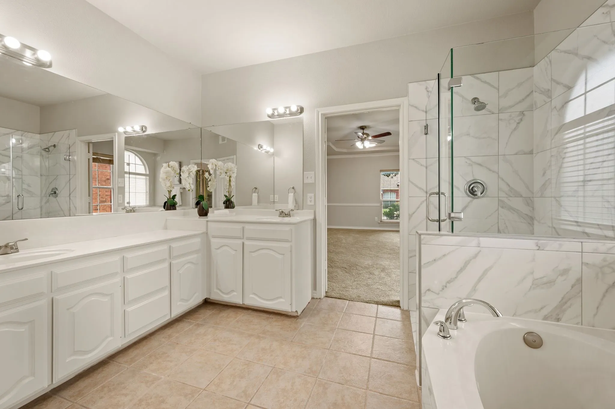 Luxurious primary bathroom featuring dual vanities with white cabinetry, marble-look countertops, and polished chrome fixtures