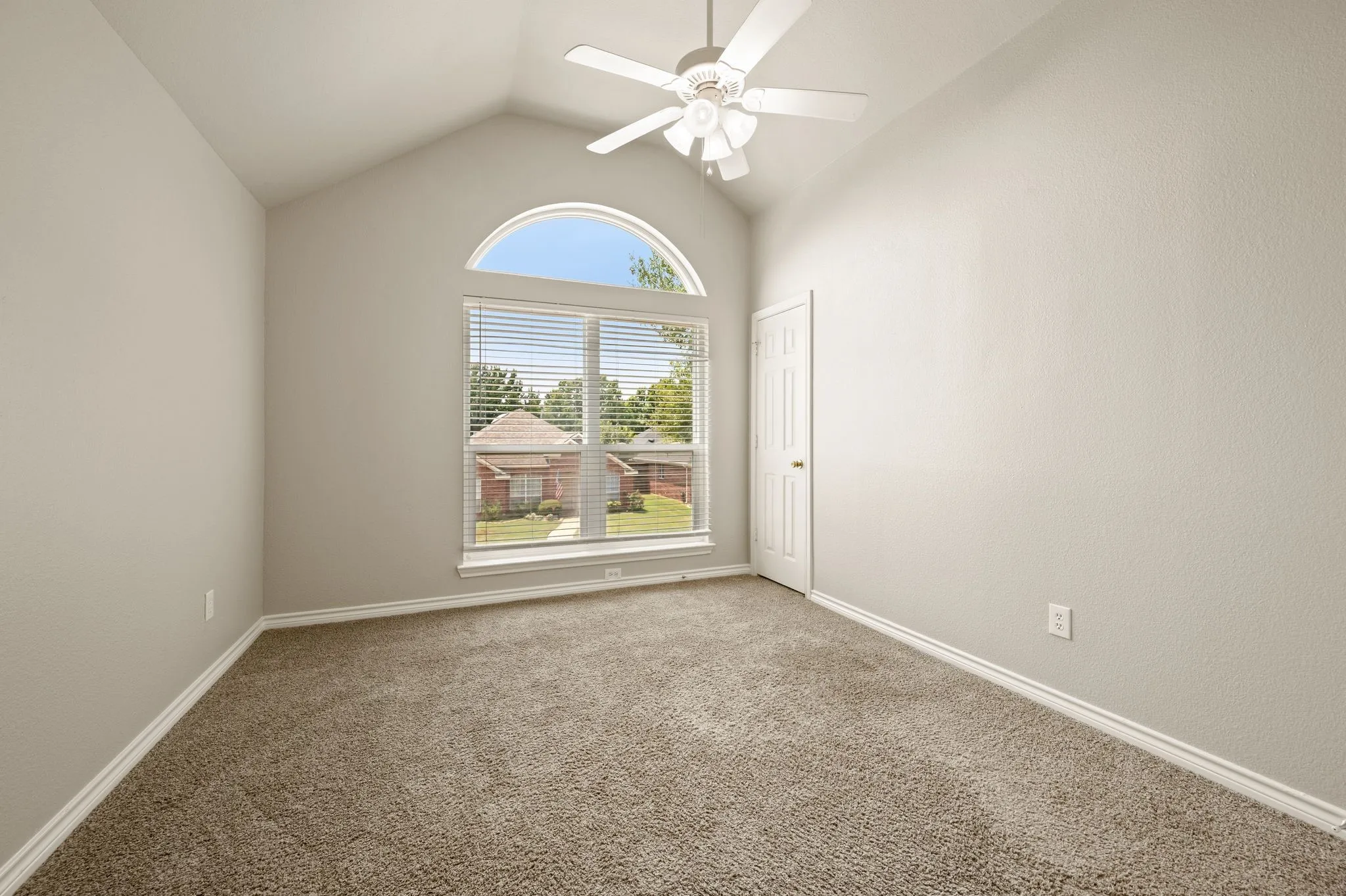 Bright secondary bedroom showcasing an arched transom window with dual-pane glass, neutral carpet flooring, ceiling fan with integrated lighting, and fresh neutral wall finishes