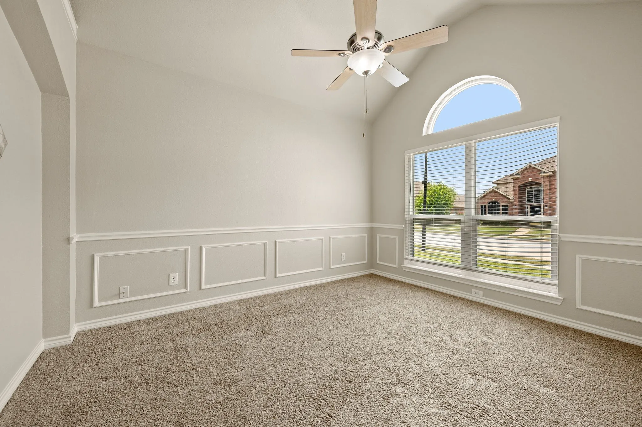 Vaulted ceiling Living Room featuring wainscoting, broad window with arched transom, and a ceiling fan with integrated lighting