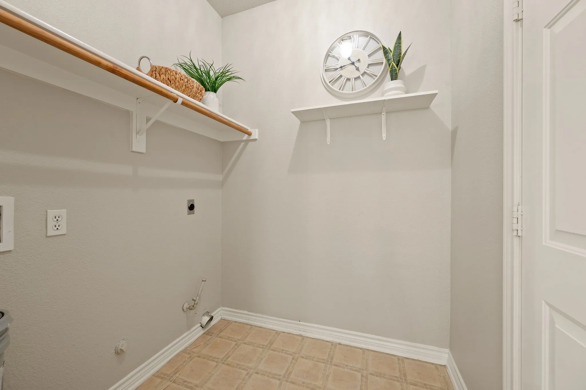 Dedicated laundry area featuring a built-in shelf with a clothing rod, a secondary floating shelf, patterned tile-finish flooring, and a paneled interior door