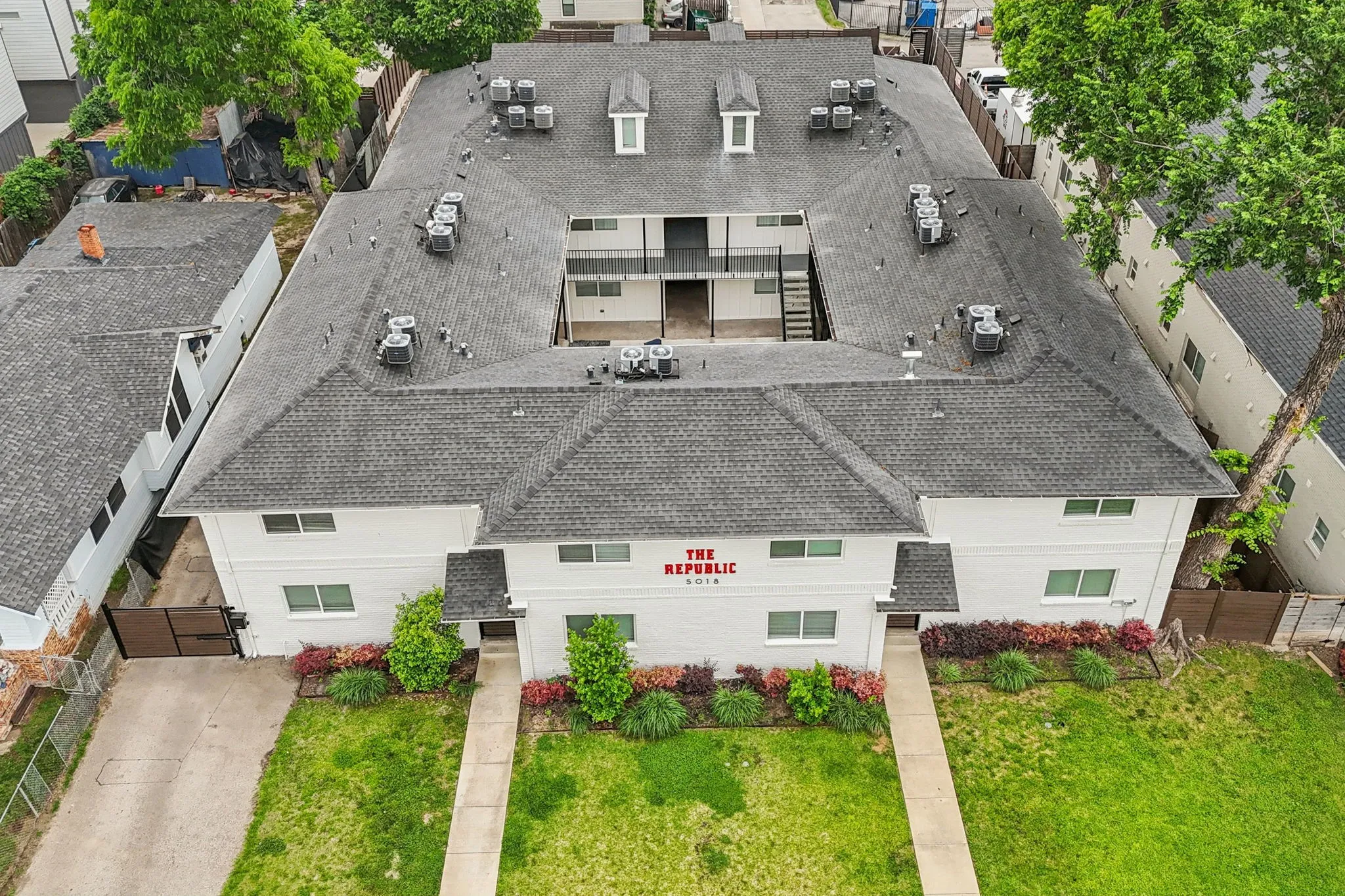 Two-story building featuring a central courtyard, multiple entry points, a gray shingle roof, and established landscaping