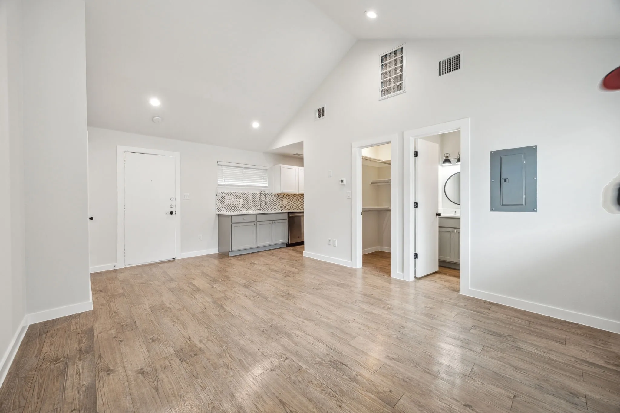 Vaulted ceiling, recessed lighting, wood-finish flooring, kitchen area with light gray cabinetry, and a walk-in closet