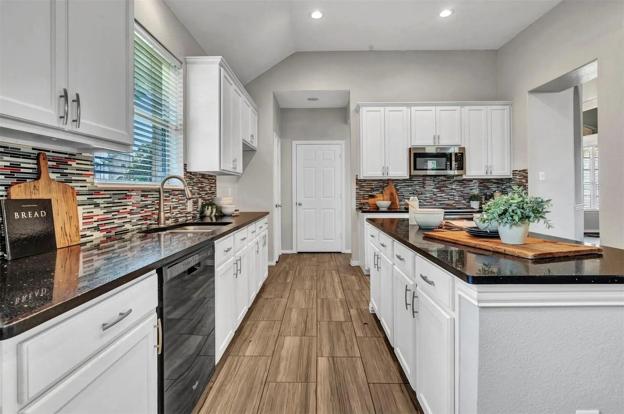Kitchen featuring white cabinetry, dark countertops, a multi-colored tile backsplash, stainless steel appliances, and wood-finish flooring