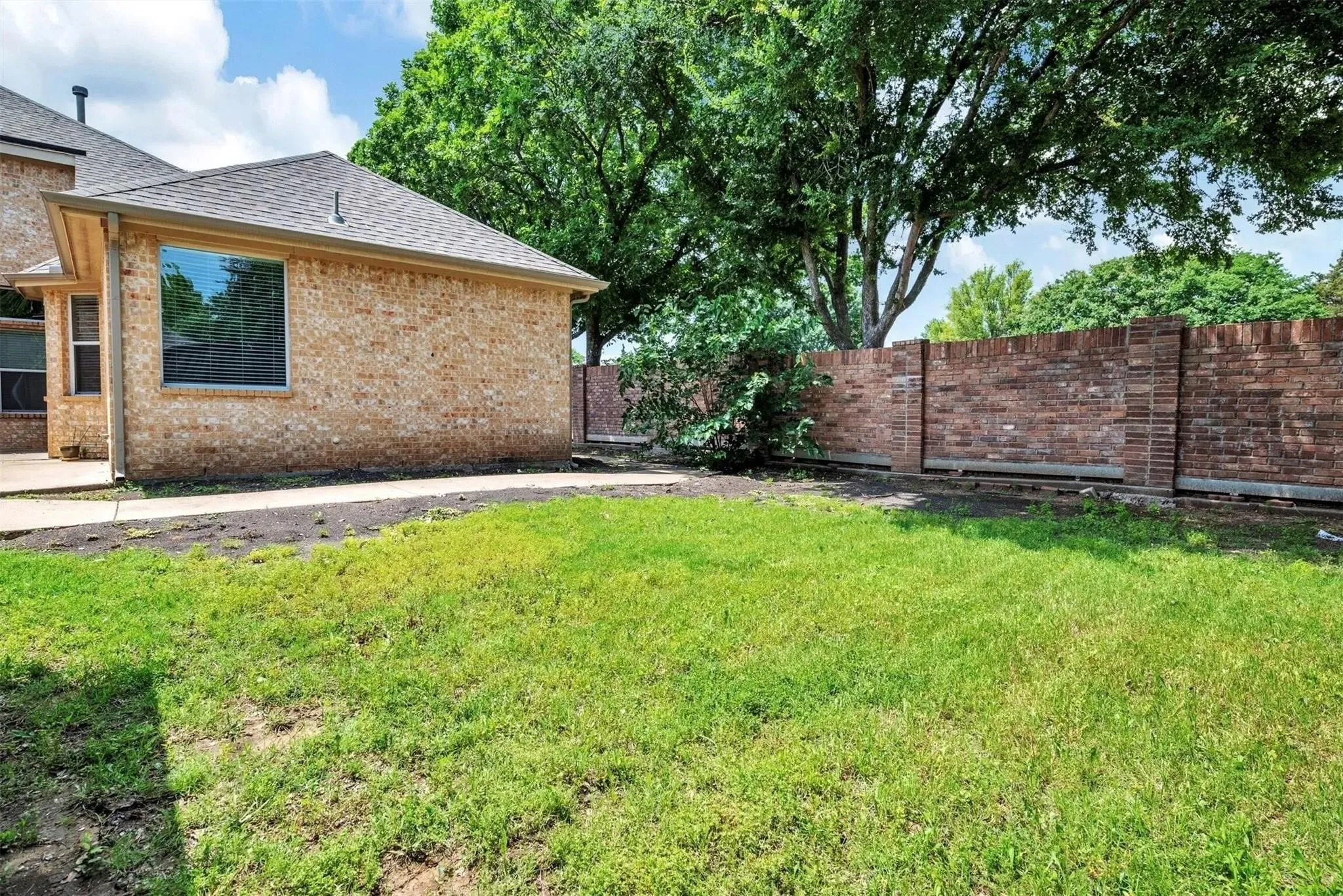 Brick exterior with a gabled roof, a large window, a concrete patio, and a brick privacy wall
