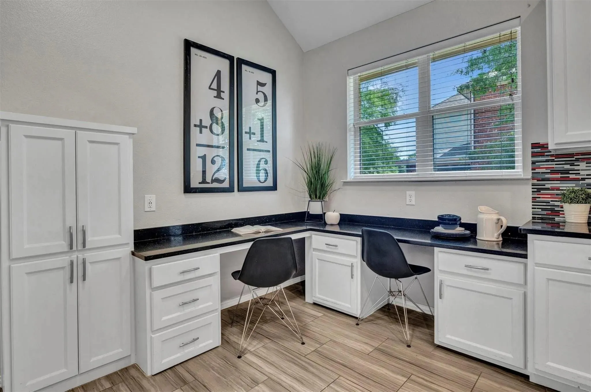 Built-in desk area with white cabinetry, dark countertops, and wood-finish flooring