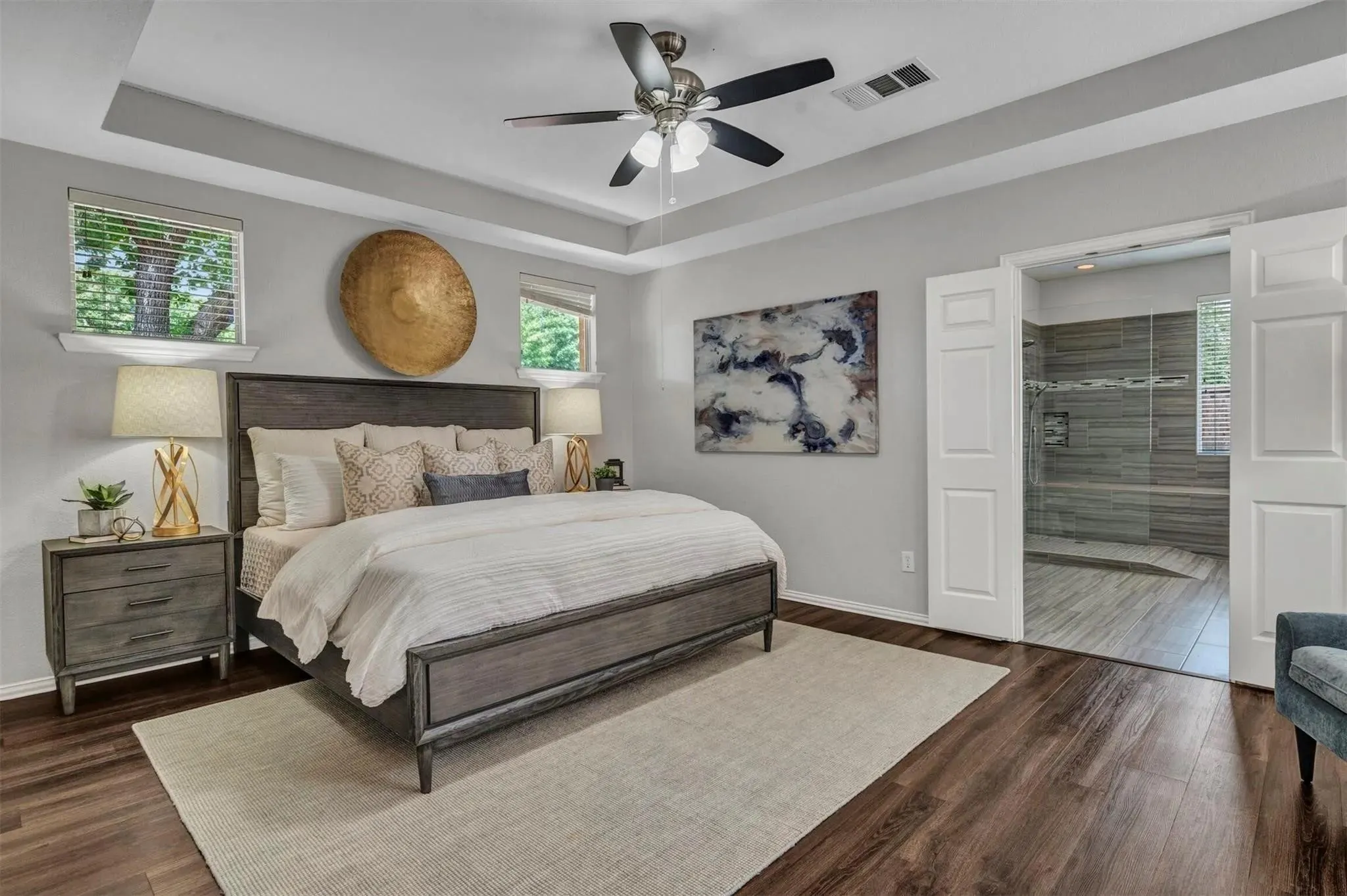 Tray ceiling with a ceiling fan, dark wood-finish flooring, two windows with blinds, and white double doors opening to a shower with glass enclosure