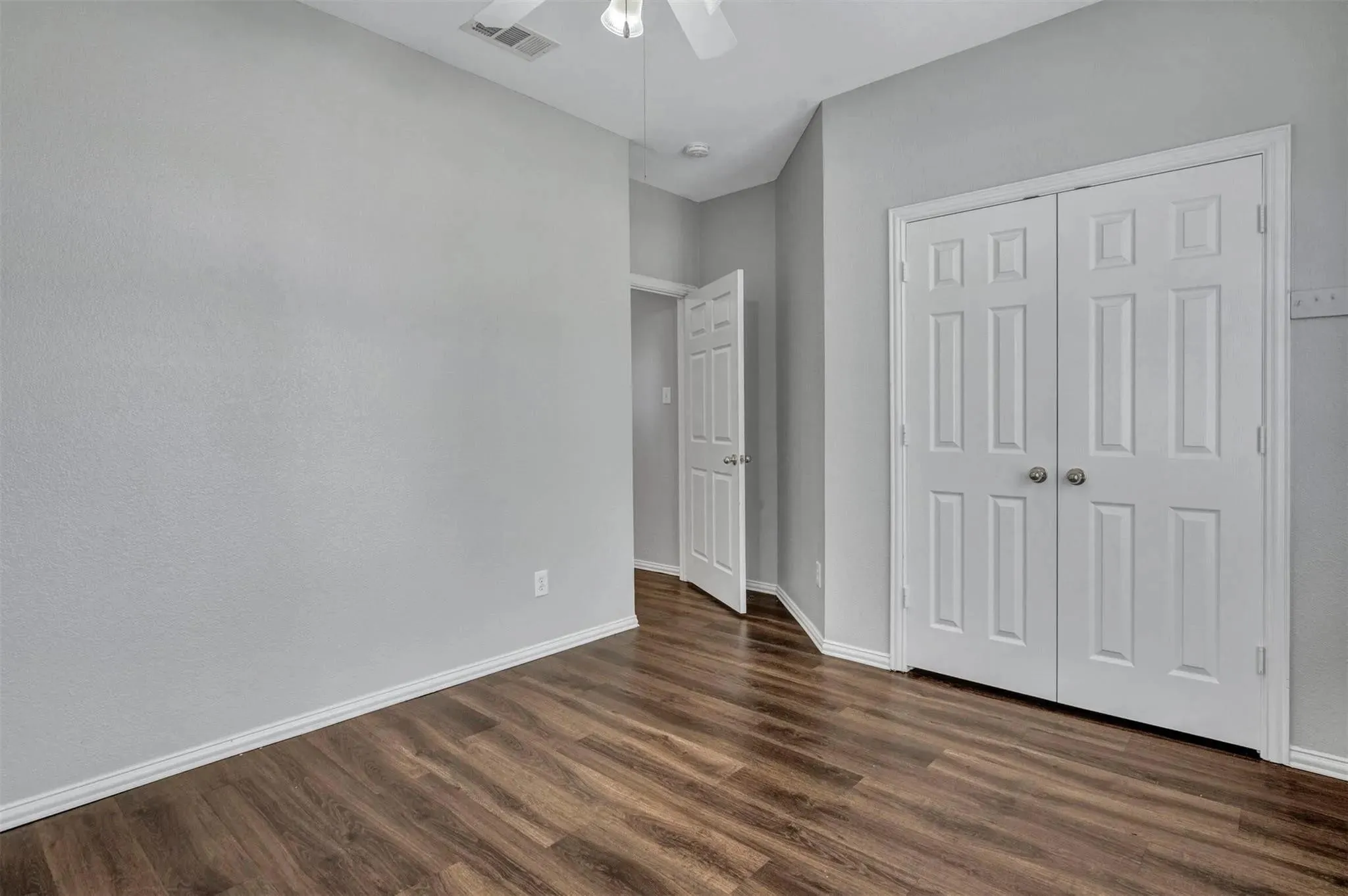 Spacious bedroom with warm wood-finish flooring, neutral painted walls, and abundant natural light