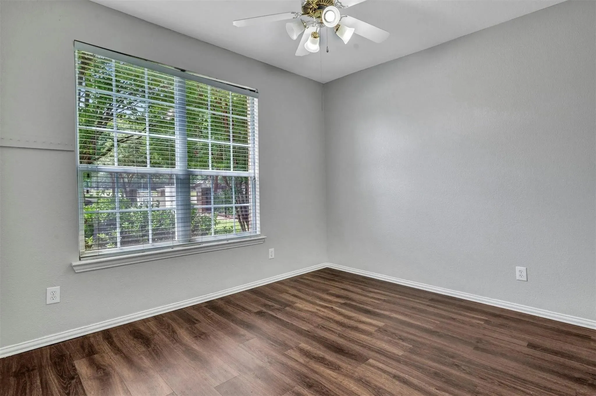Wood-finish flooring, ceiling fan with integrated lighting, window with blinds, and light gray wall finish