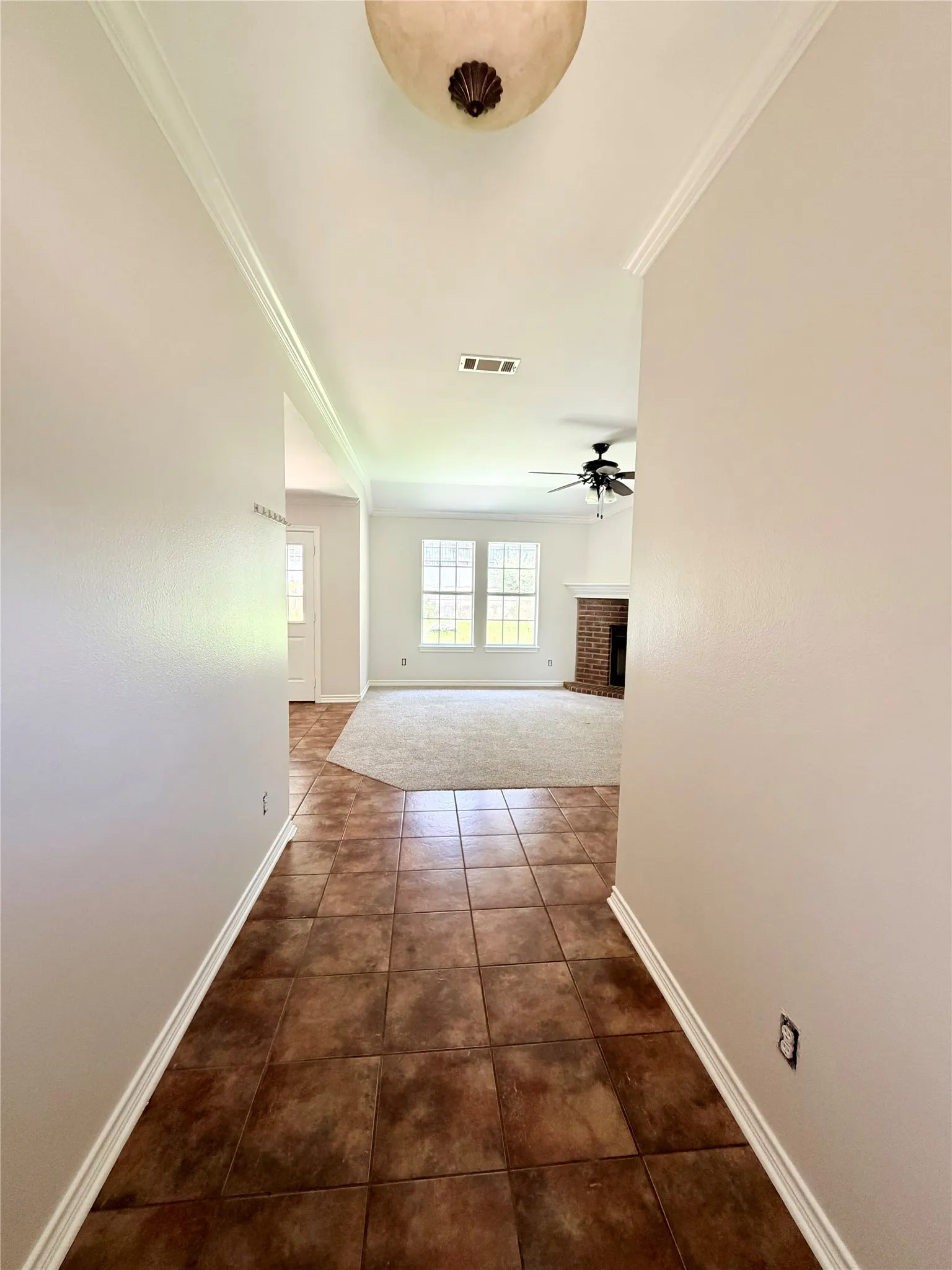Foyer with tile flooring leading to an open living area featuring carpet, multiple windows, a ceiling fan, and a fireplace with a brick surround