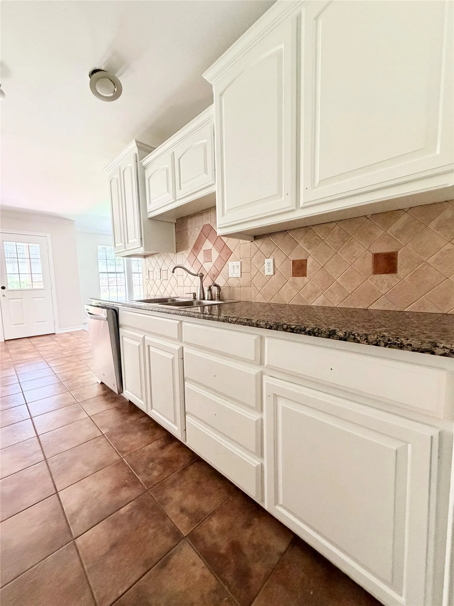 White cabinetry, granite-style countertops, tile backsplash with accent squares, stainless steel sink, and tile flooring
