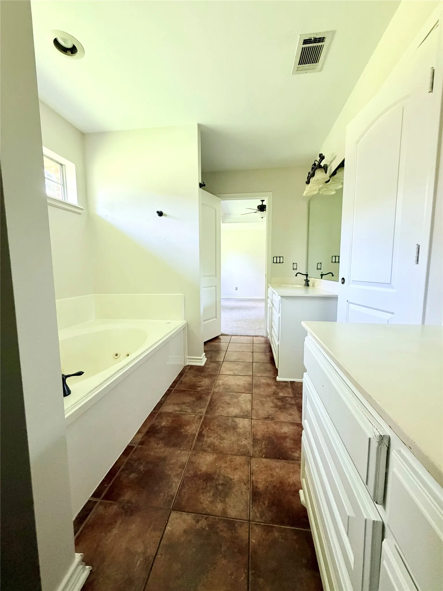 Built-in soaking tub, dual vanity with undermount sinks, white cabinetry, and large format floor tile
