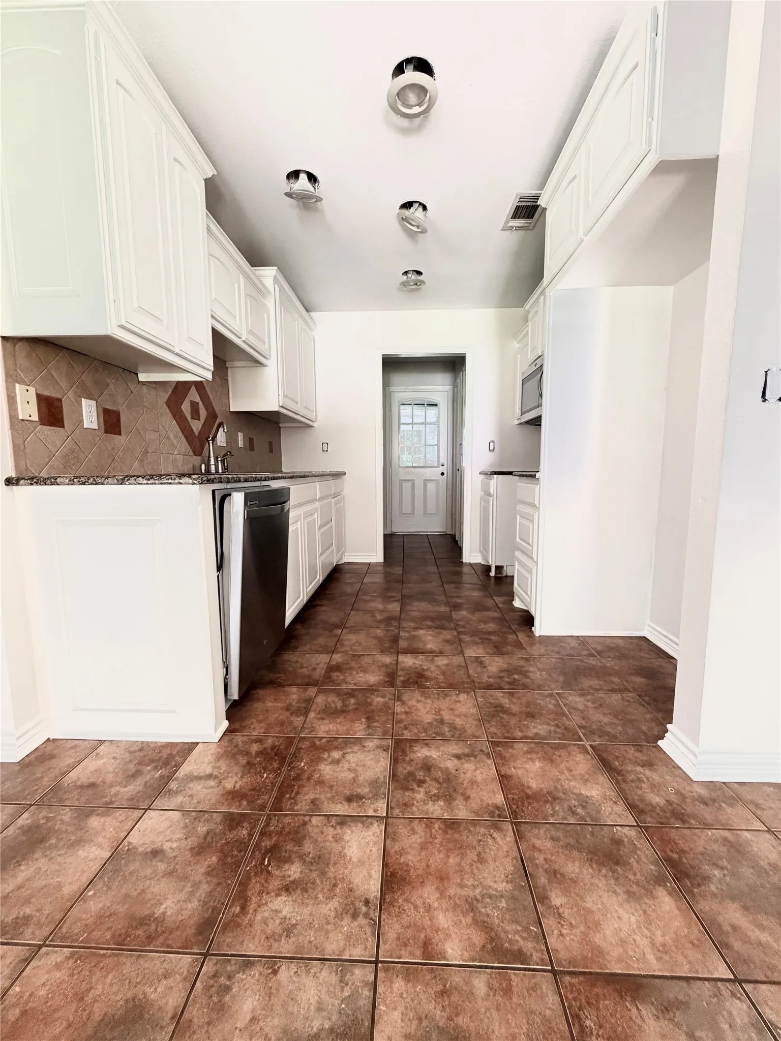 White shaker-style cabinetry with crown molding, granite countertops, tile backsplash with accent inserts, stainless steel dishwasher, and large format tile flooring