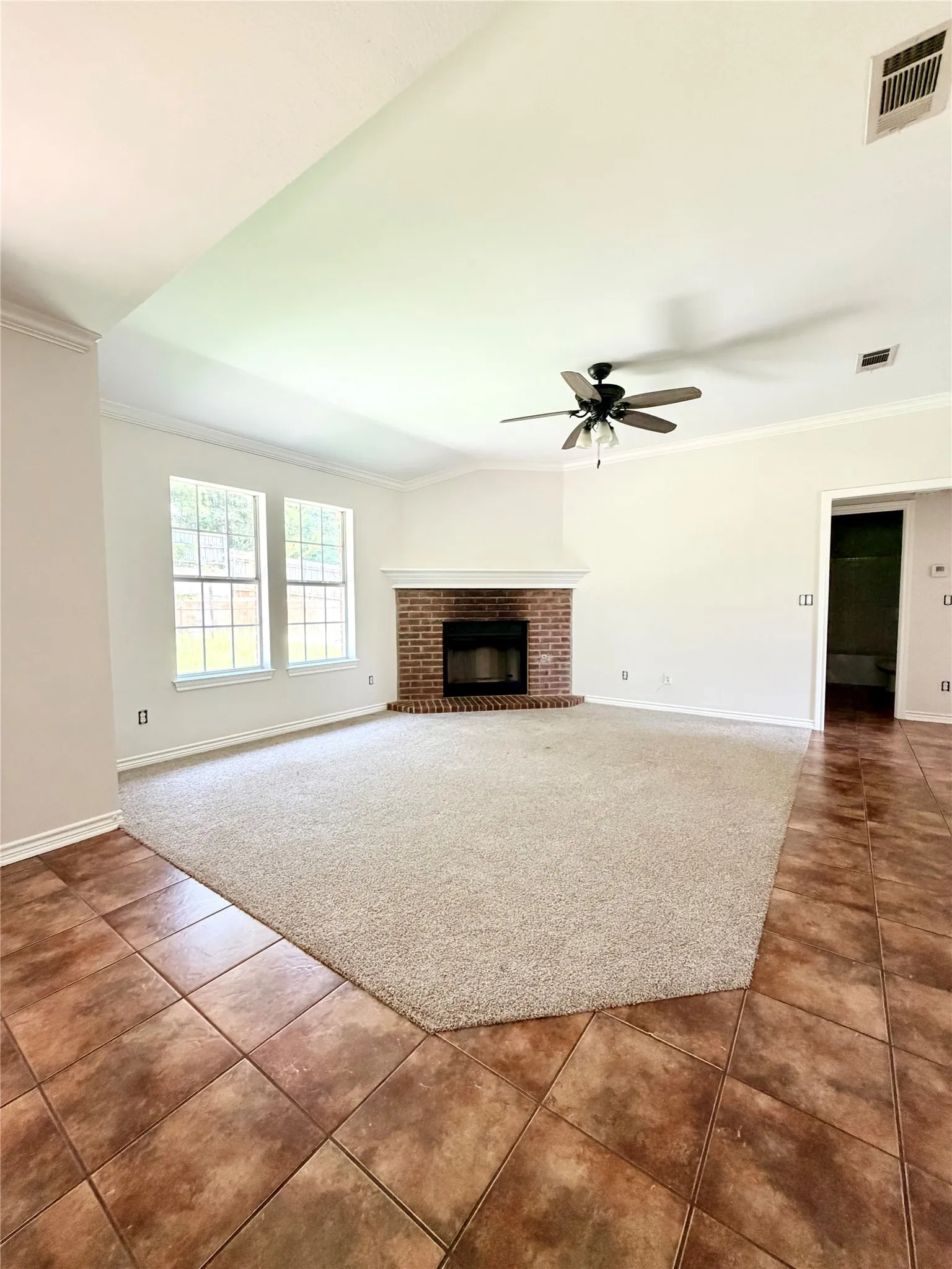 Vaulted ceiling with a ceiling fan, brick-surround fireplace with a white mantel, and multiple windows