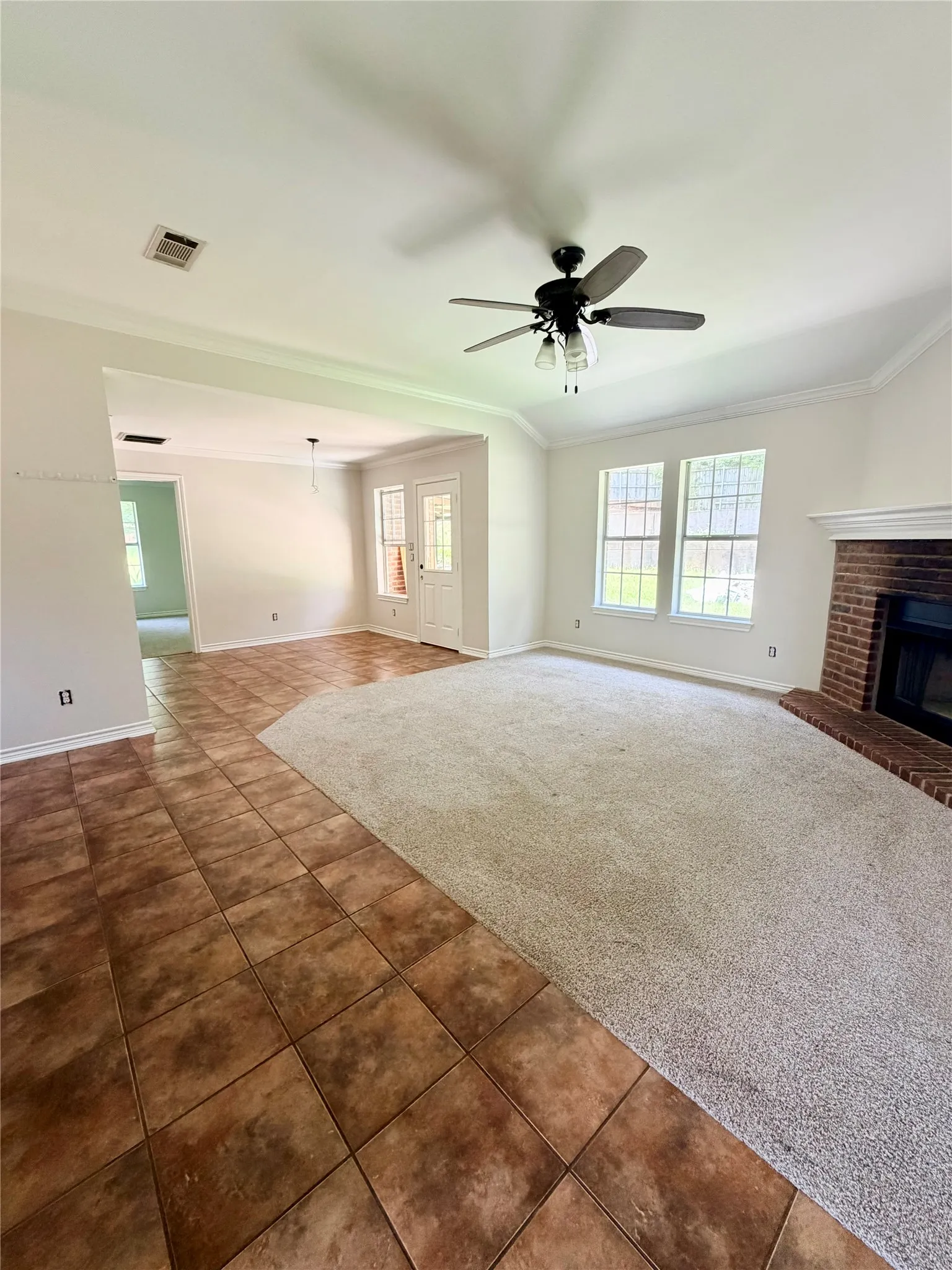 Spacious living area featuring a brick fireplace, ceiling fan with light kit, multiple windows, and crown molding